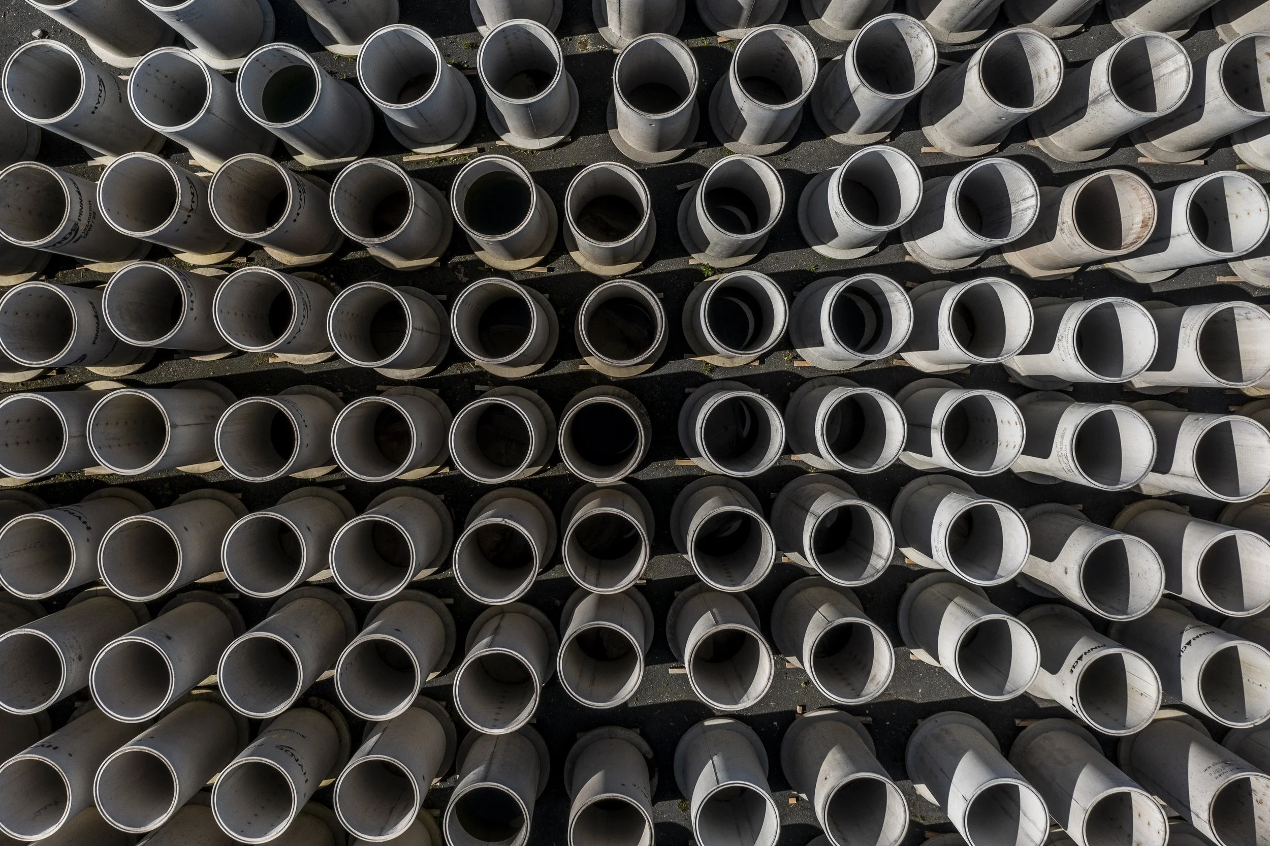 Aerial view of stacked white PVC pipes arranged in parallel rows on wooden supports.