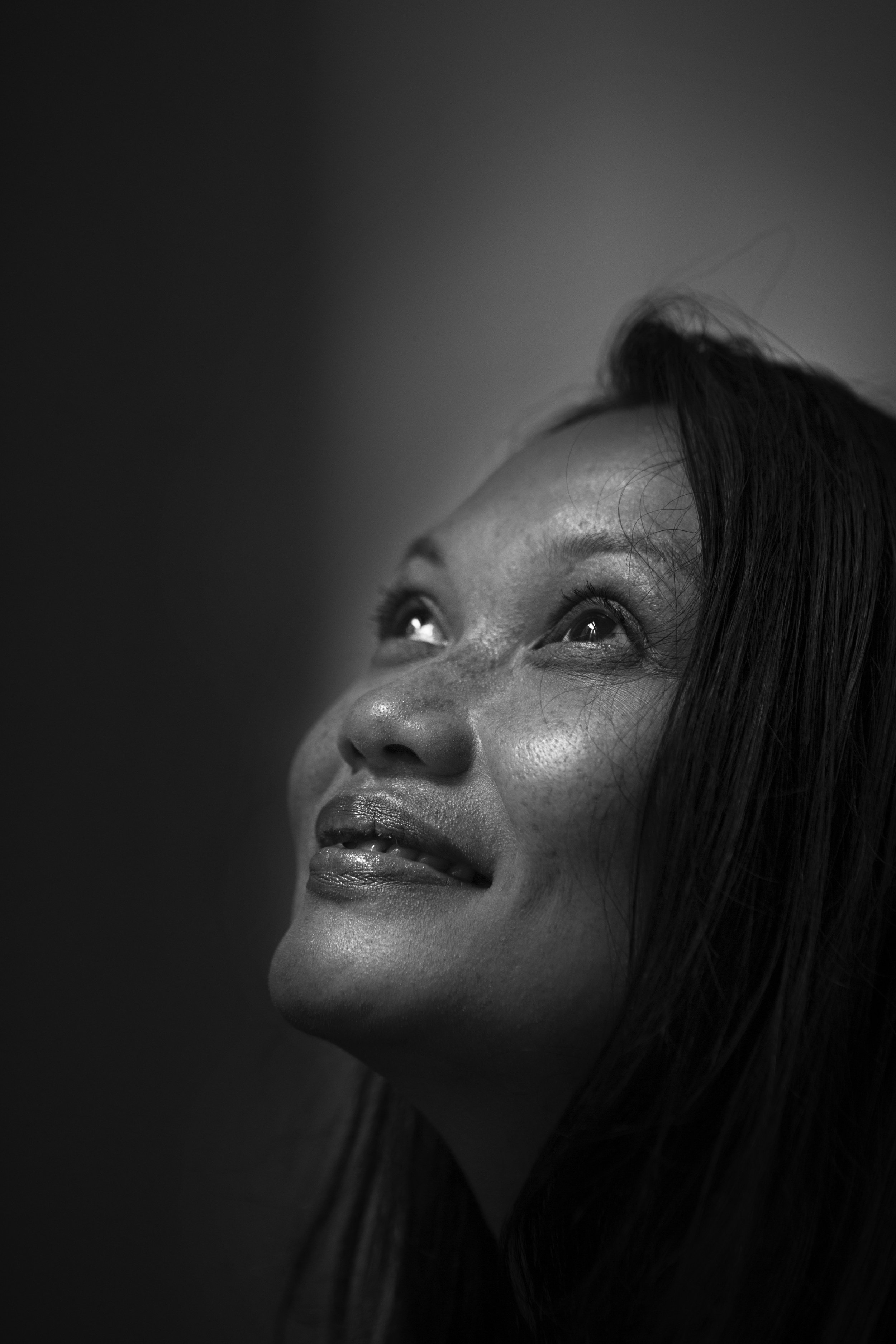 Close-up black and white portrait of a smiling woman looking upward, with a soft glow highlighting her facial features.