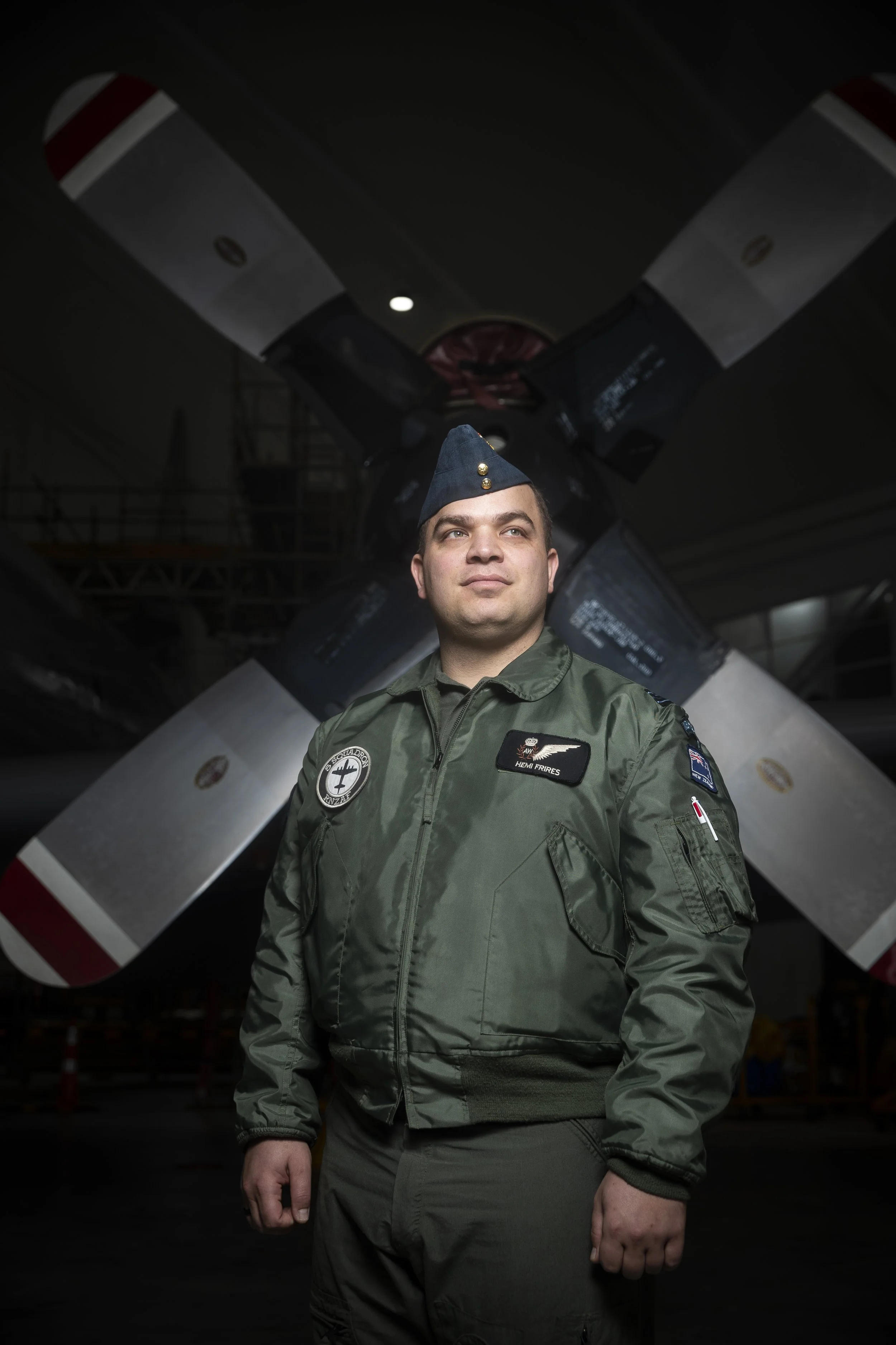 A male pilot in a military uniform standing in front of a helicopter with a large rotor in the background.