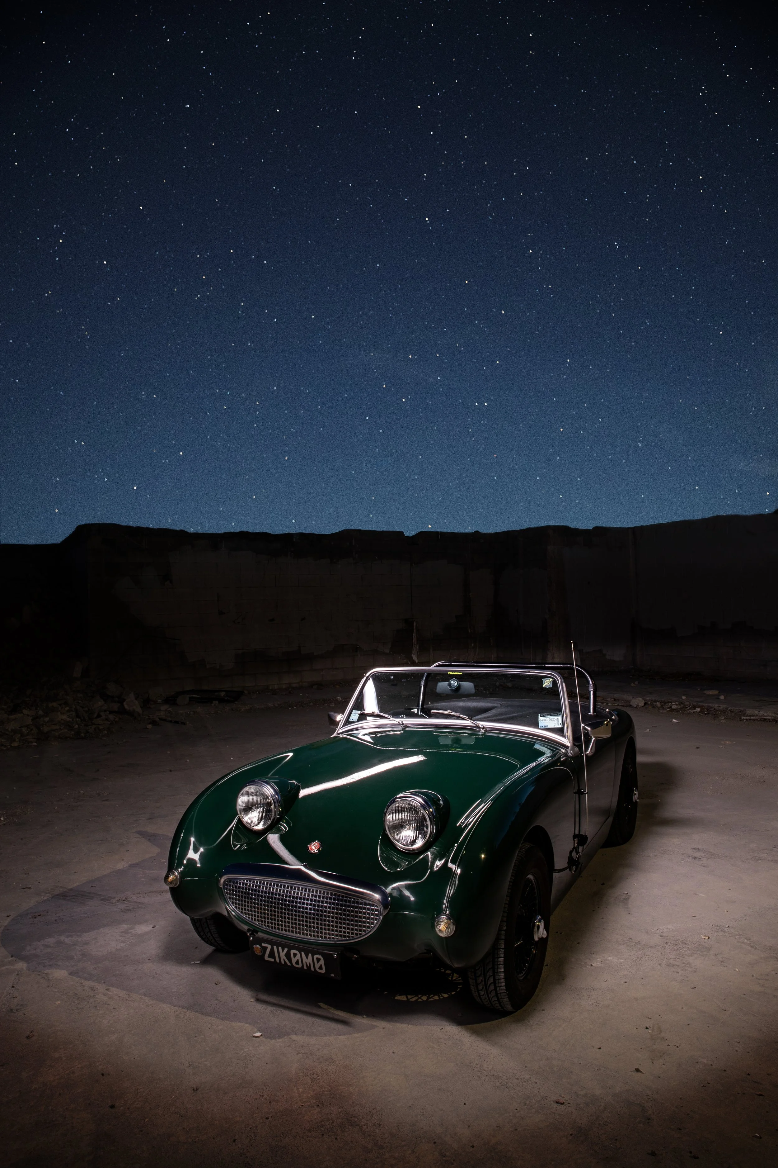 A vintage green convertible car parked on a flat surface at night under a starry sky.
