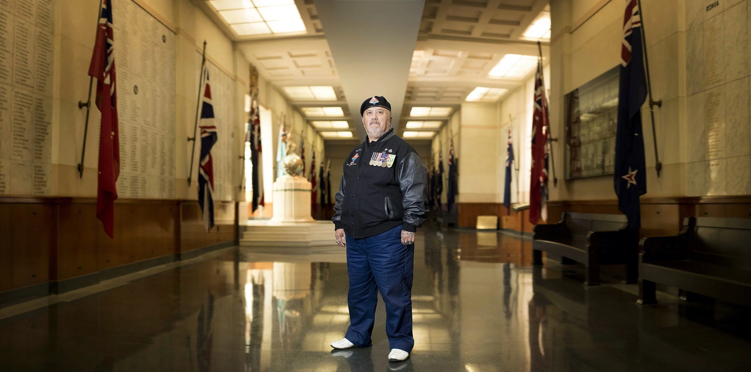 A man in a military uniform with medals standing in a hallway decorated with flags and murals.