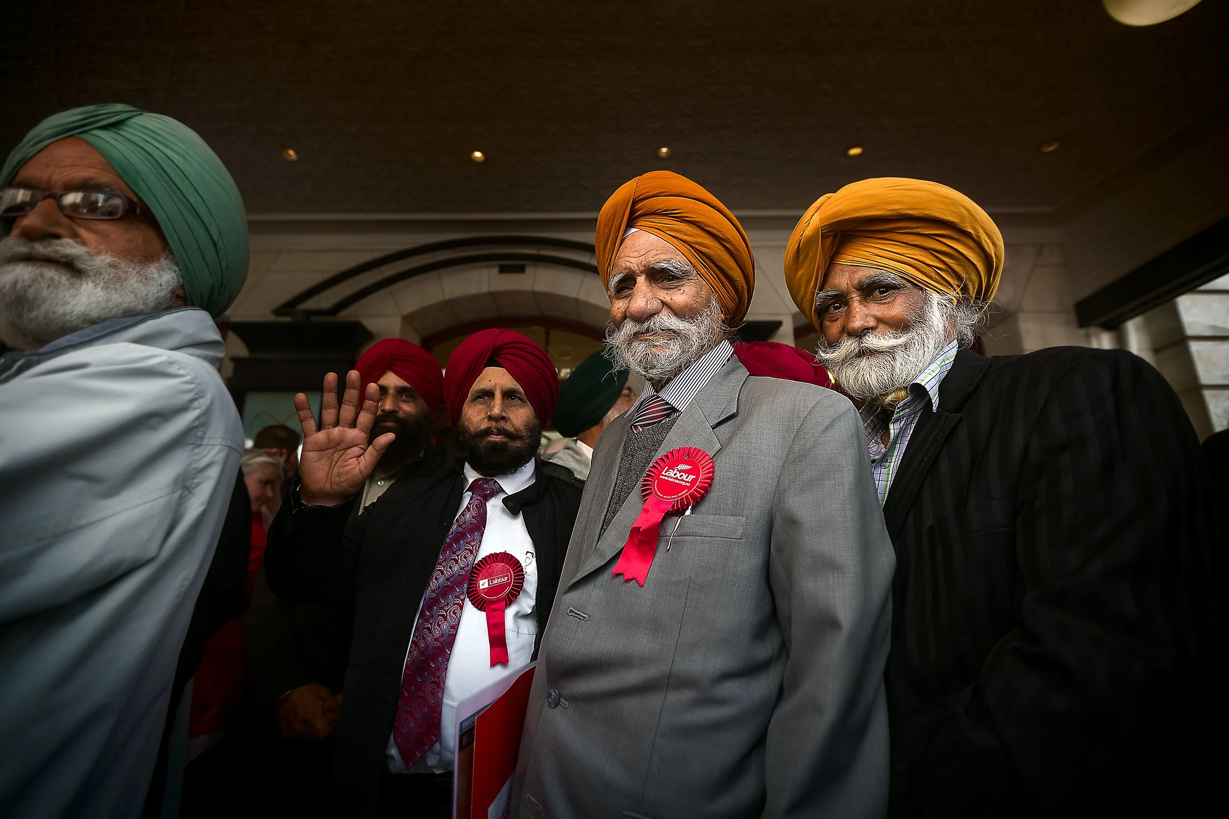 Group of Indian men, wearing traditional turbans and suits, attending a political event with Labour party badges.