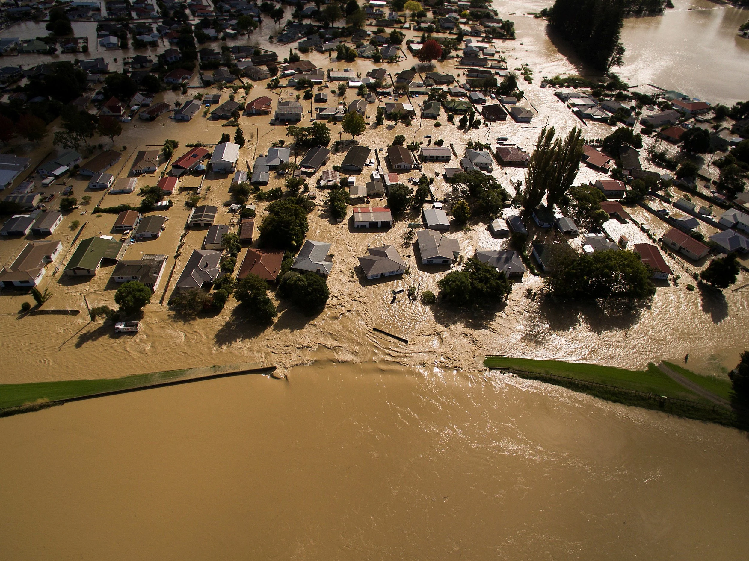 Aerial view of a neighborhood flooded with muddy water, with many houses partially submerged and debris floating on the surface.