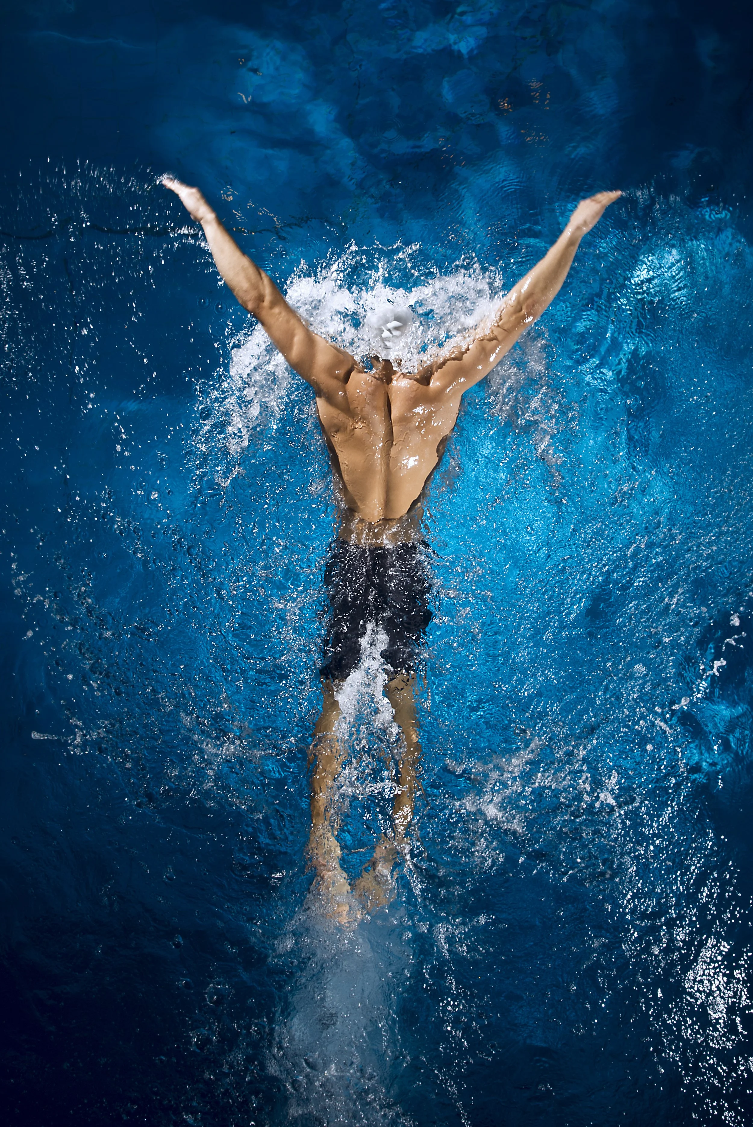 A swimmer submerged in water with arms extended upward and creating a splash.