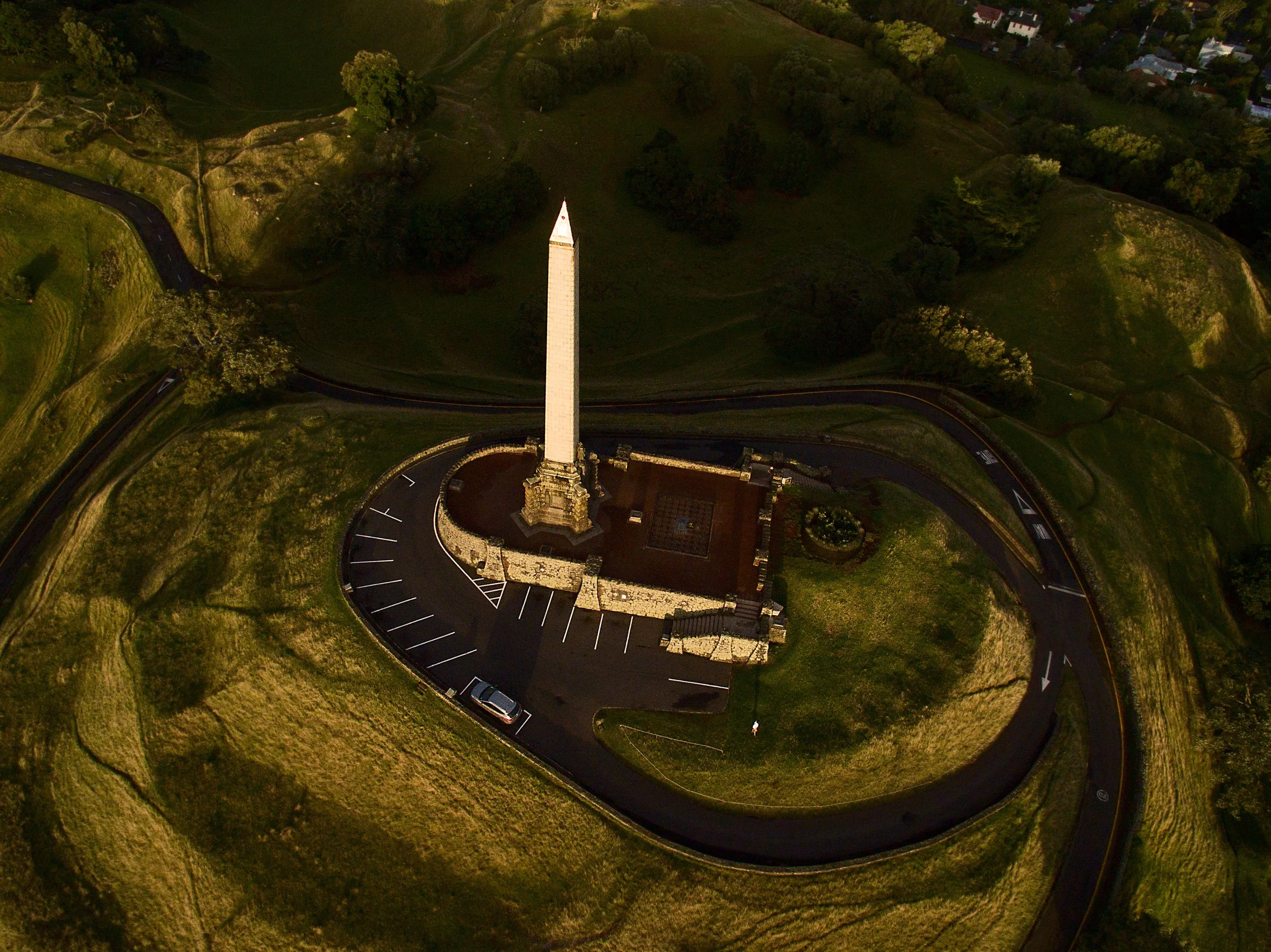 An aerial view of the Washington Monument situated on a grassy hill with a curved driveway and parking lot surrounding it.