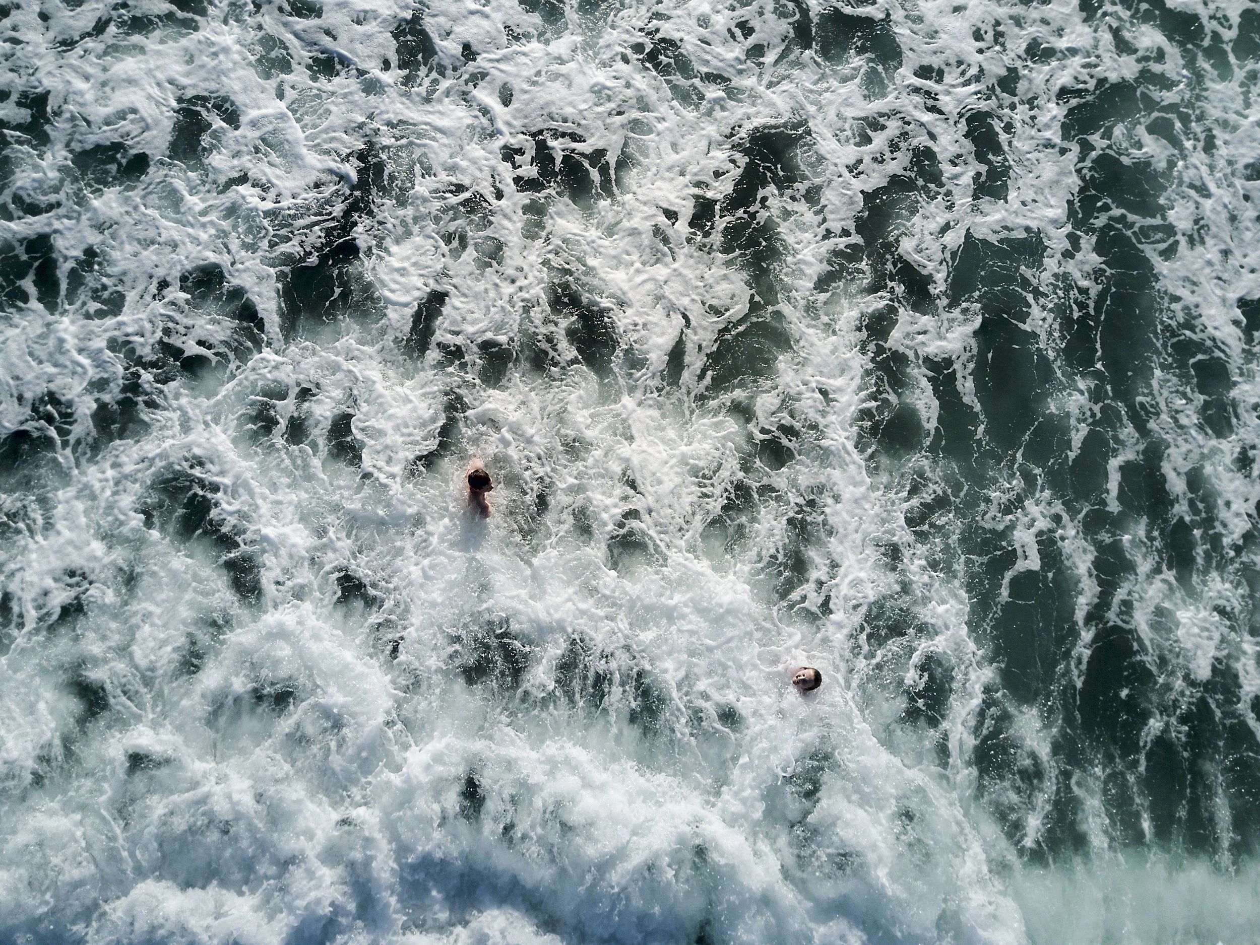 Overhead view of ocean waves with two swimmers in the water.