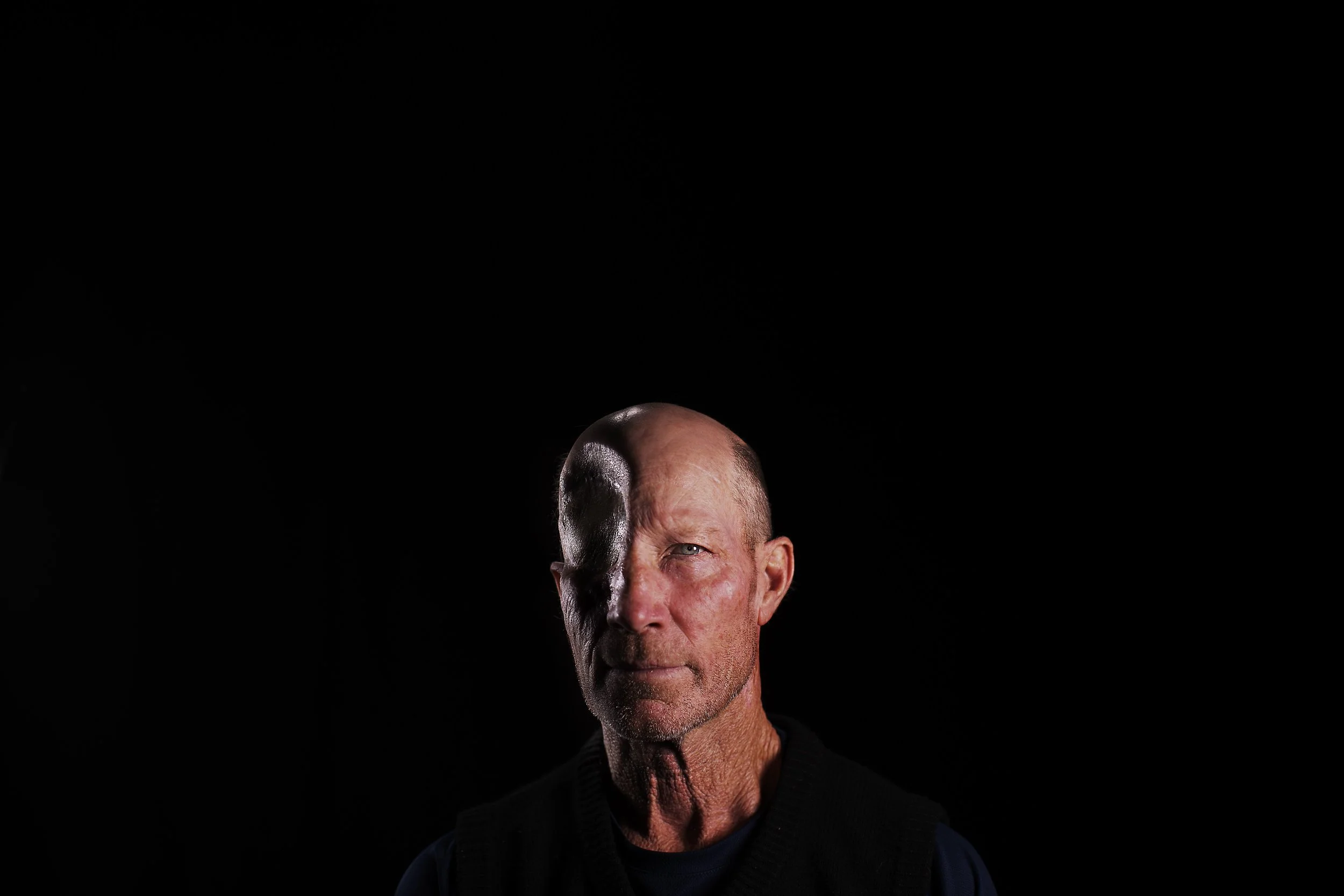 Portrait of a middle-aged man with one side of his face in shadow, against a black background.