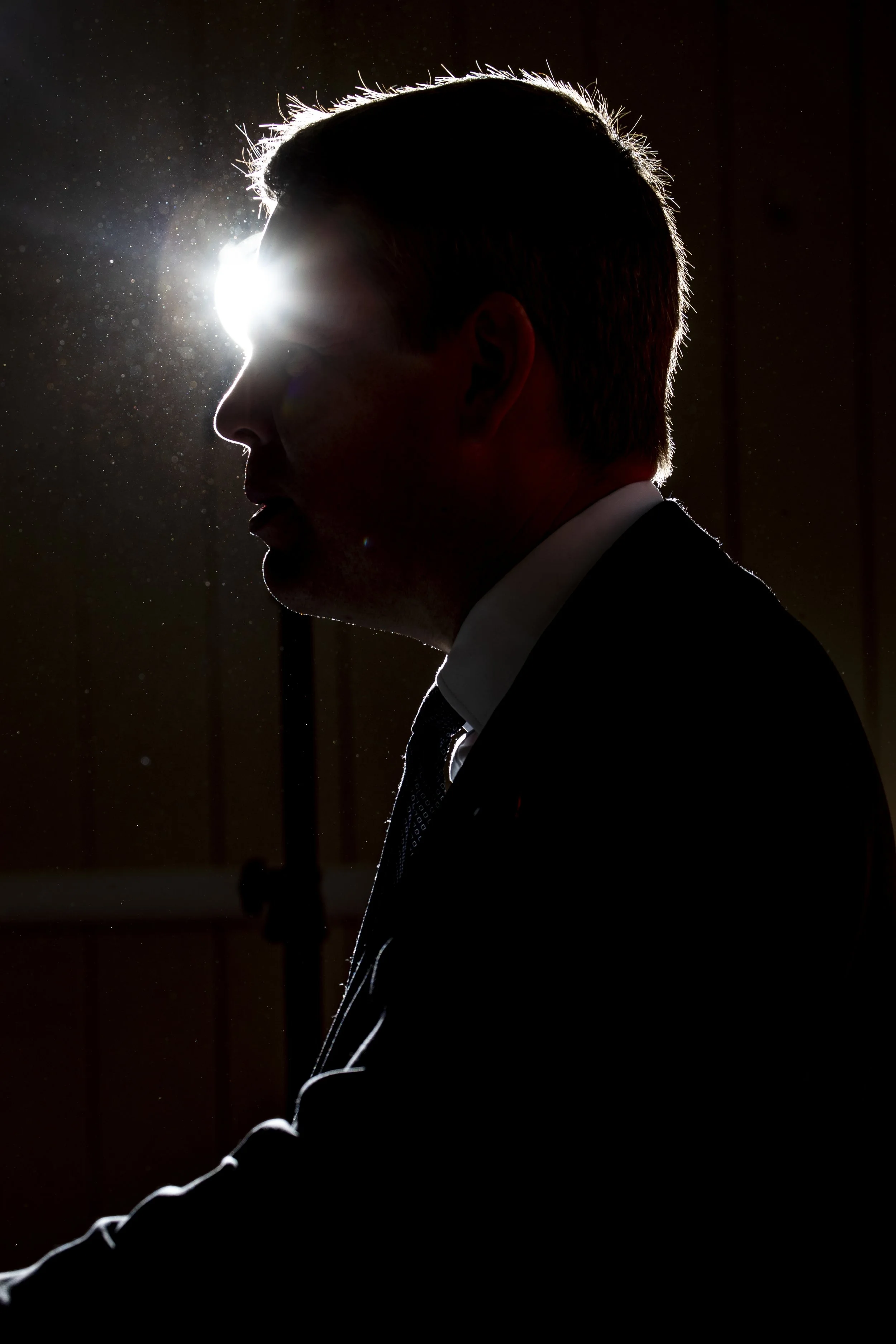 Silhouette of a man in a suit and tie, with a bright light source behind him creating a halo effect on the edges of his head and shoulders.