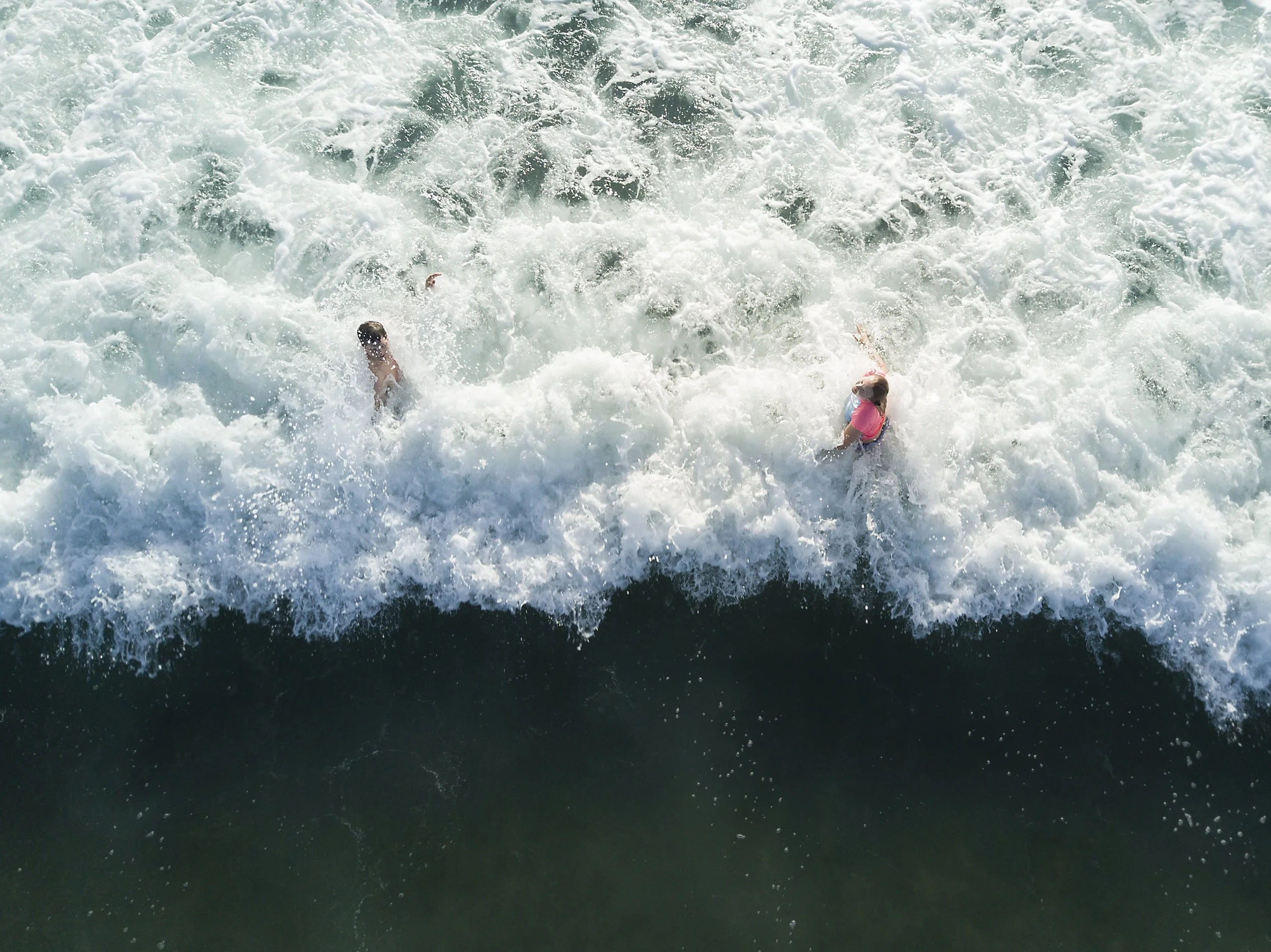 Two children playing in the ocean waves on a sunny day.