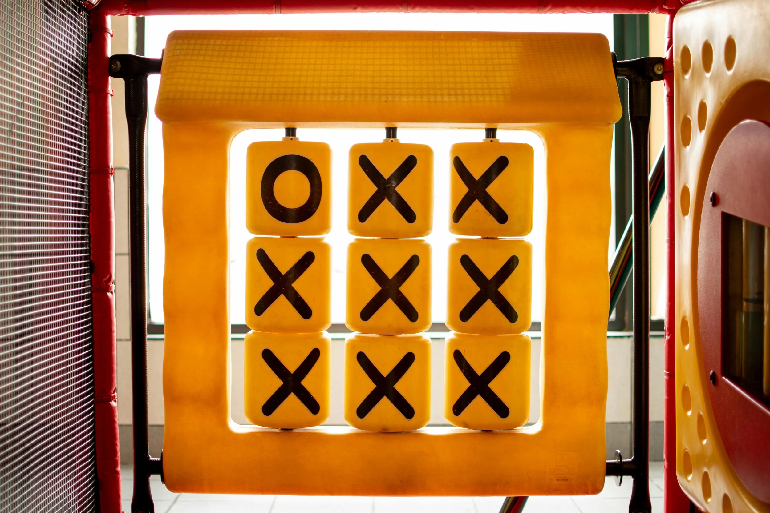 Yellow Tic-Tac-Toe game board with X's and O's on a playground structure.