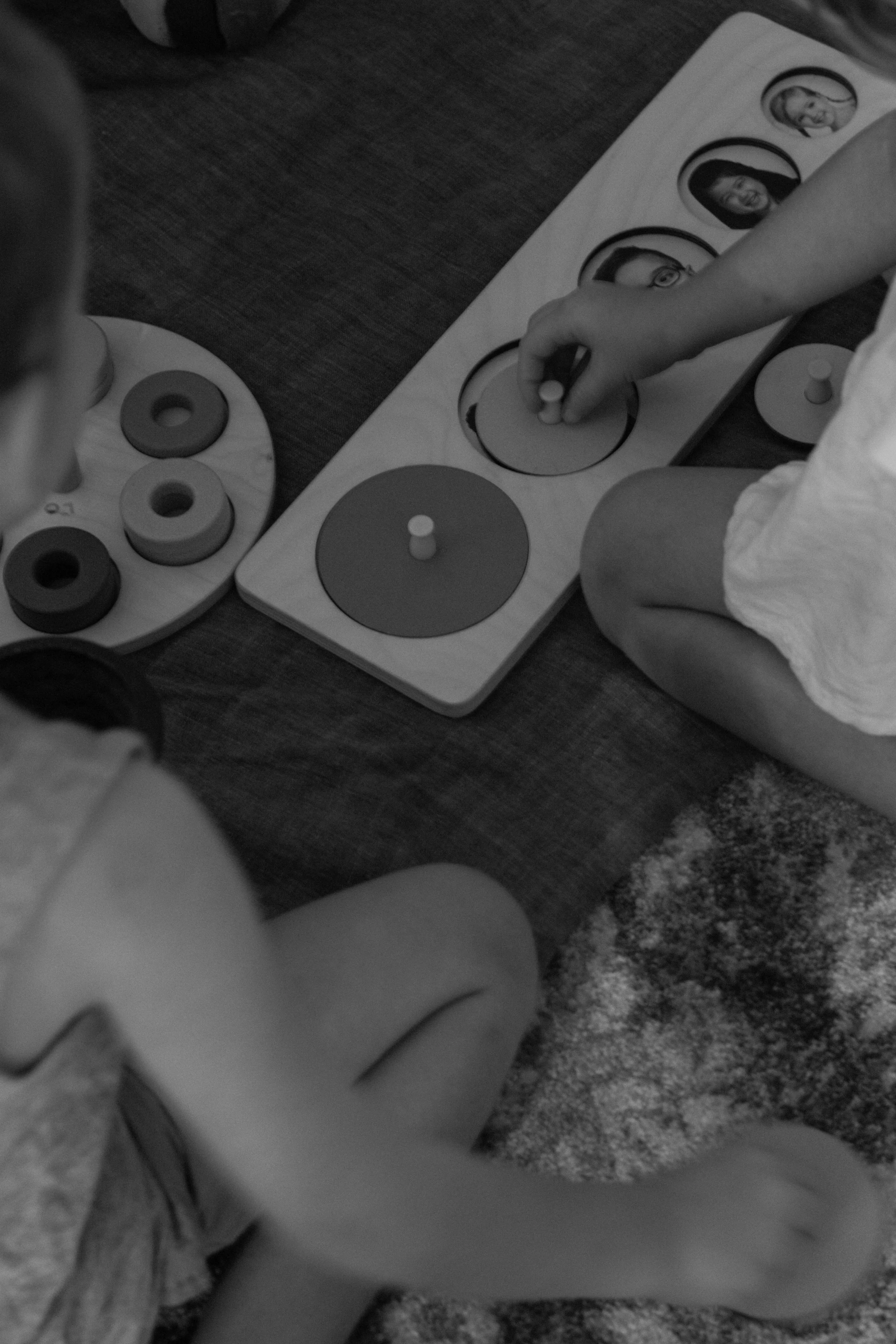 Two children playing with educational toys, one with a set of disks and the other with a picture puzzle, sitting on a rug.