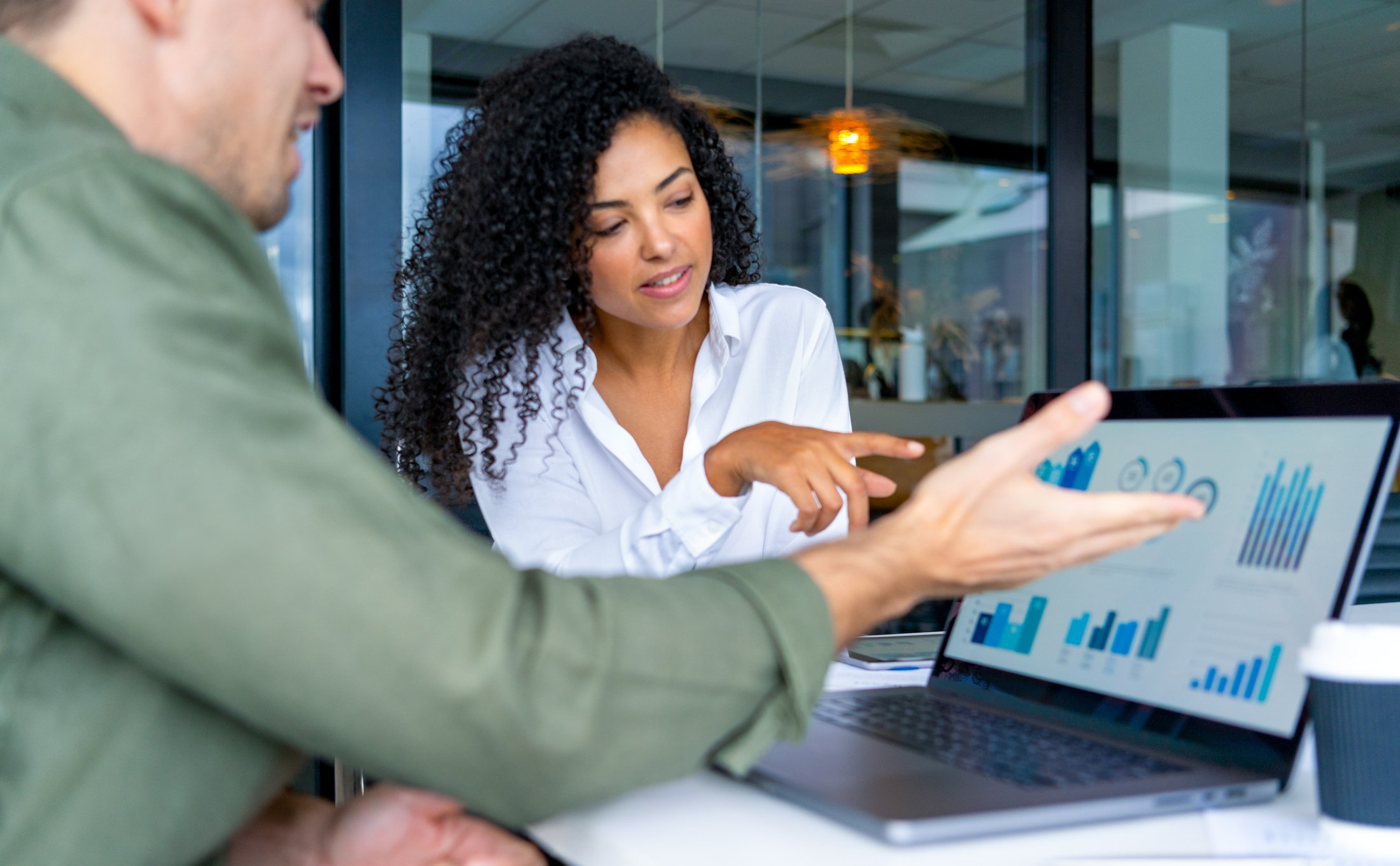Two people reviewing data and charts on a laptop and a tablet in a modern office.