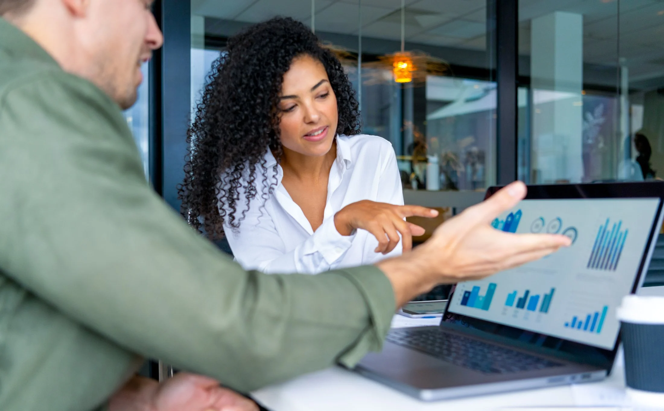 Two people discussing data on a laptop in a modern office setting, with graphs on the screen.