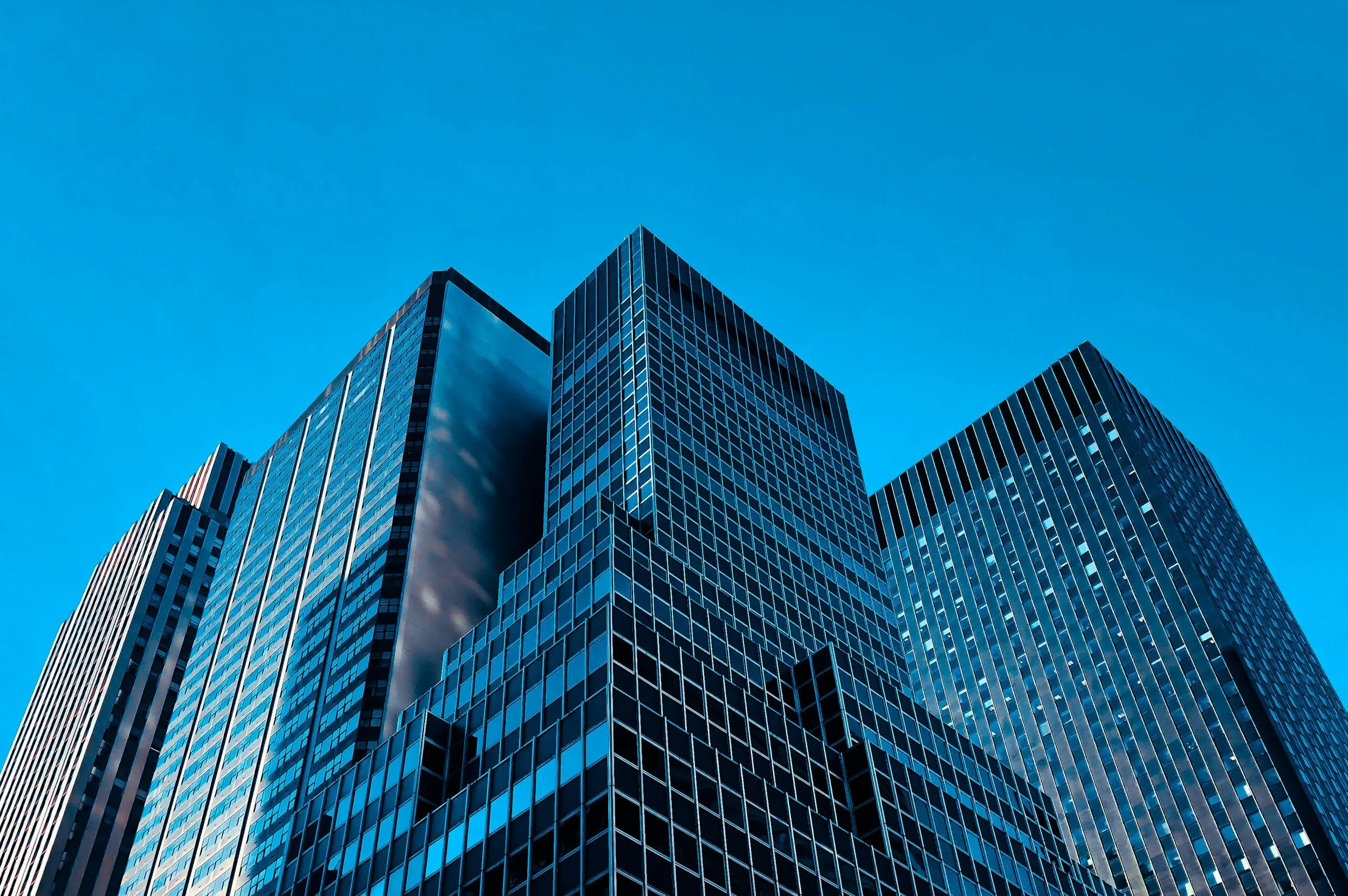 A low-angle view of modern glass skyscrapers against a clear blue sky.