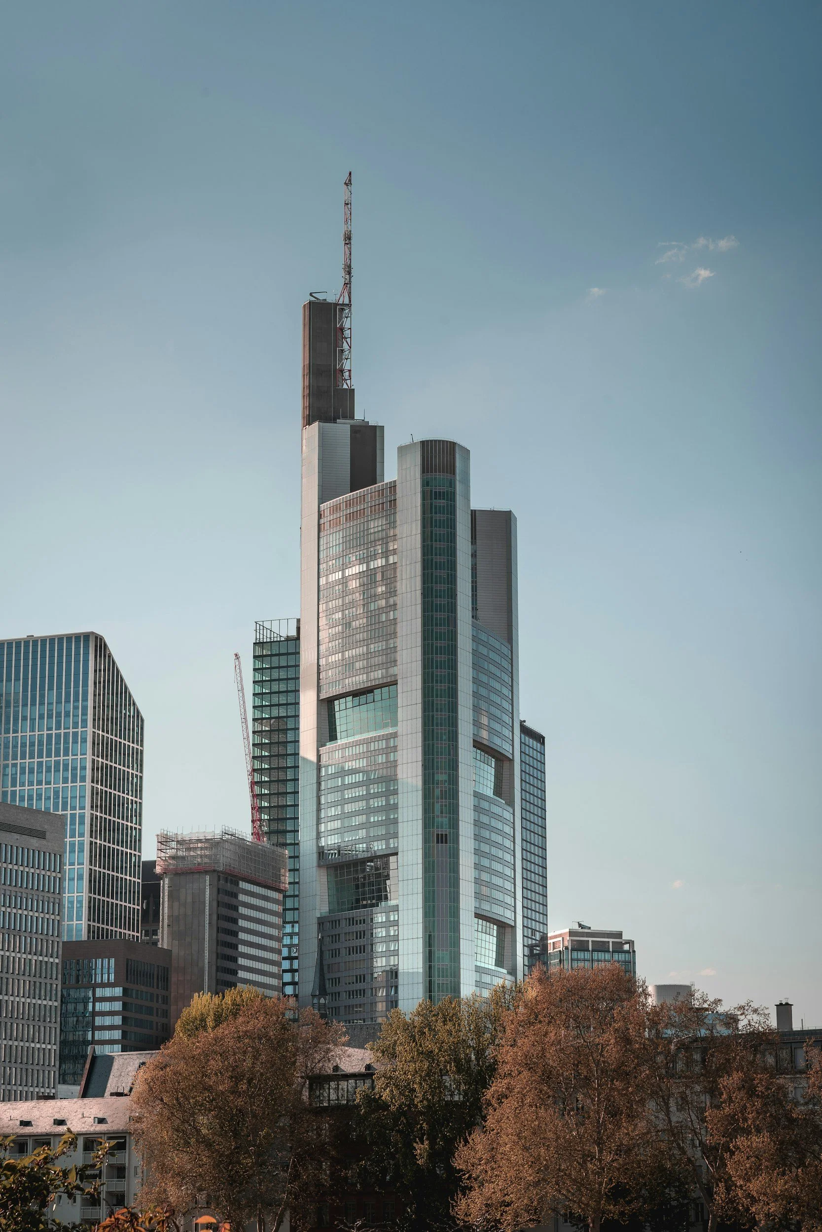 A tall, modern skyscraper with a glass exterior and multiple sections, located in an urban area with trees in the foreground.