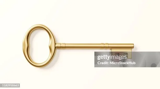 A gold-colored key with an oval-shaped handle laying on a white surface.