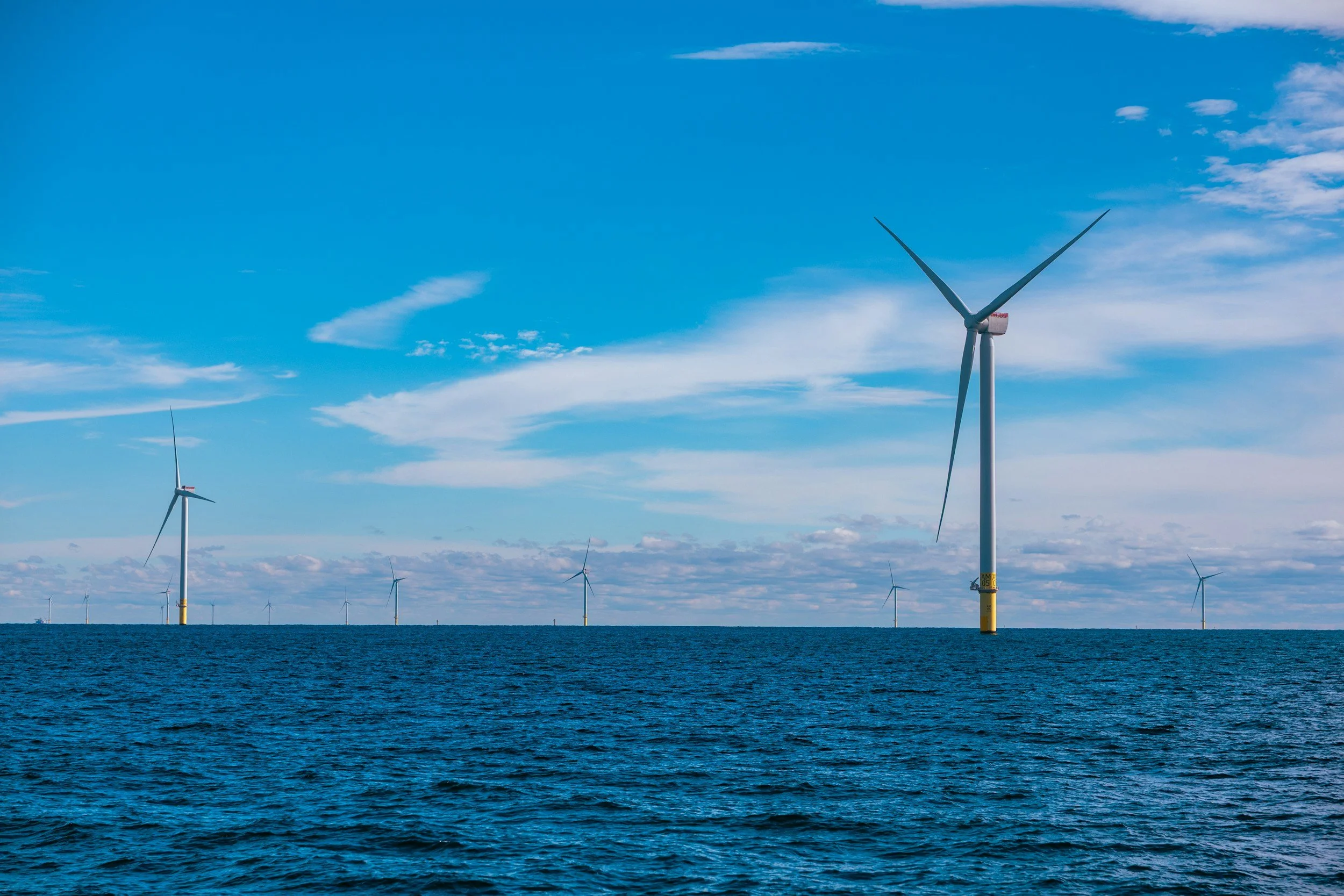 Offshore wind turbines in the ocean under a blue sky with scattered clouds.