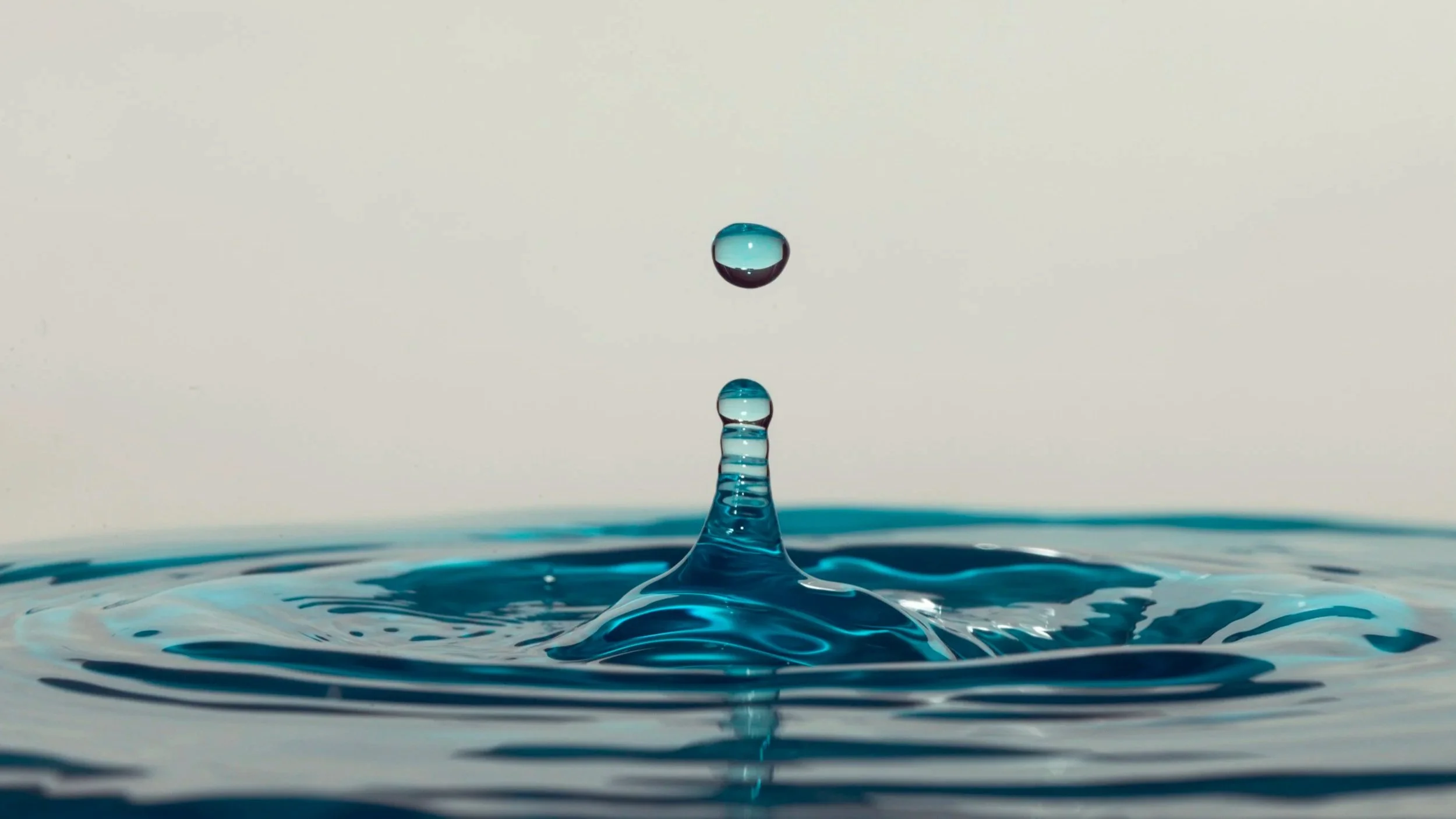 Close-up of a water droplet falling into a body of water, creating a splash and ripples.