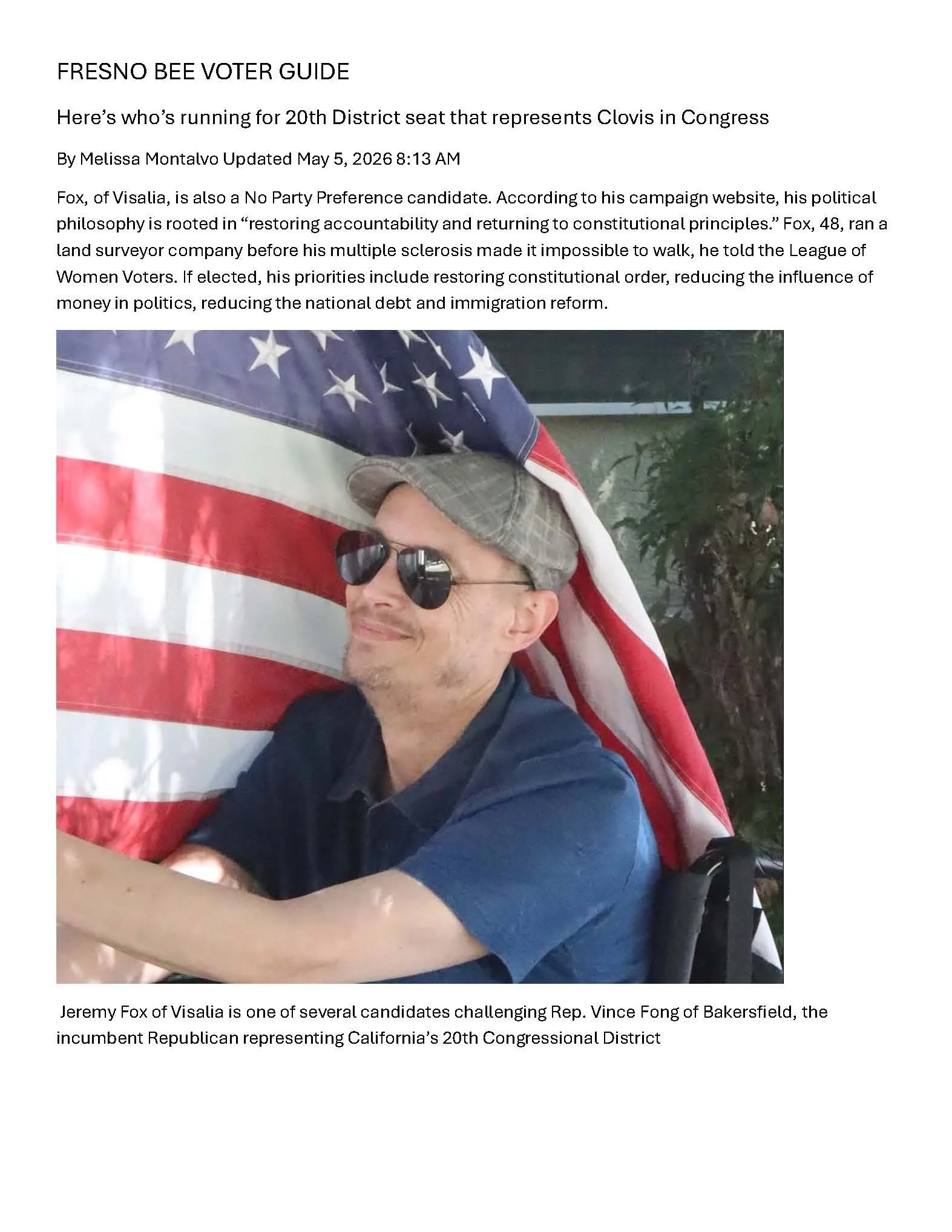 Jeremy Fox with glasses and a baseball cap is smiling while holding an American flag, with green trees in the background. Fresno Bee