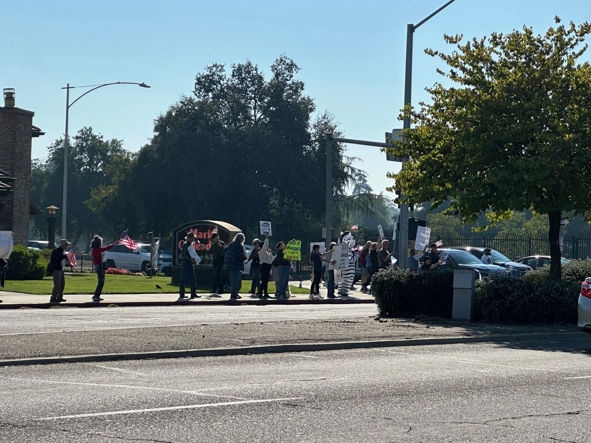 People gathered on the street holding signs and American flags, participating in a demonstration or protest outside a building with a sign that reads 'Marriott.'