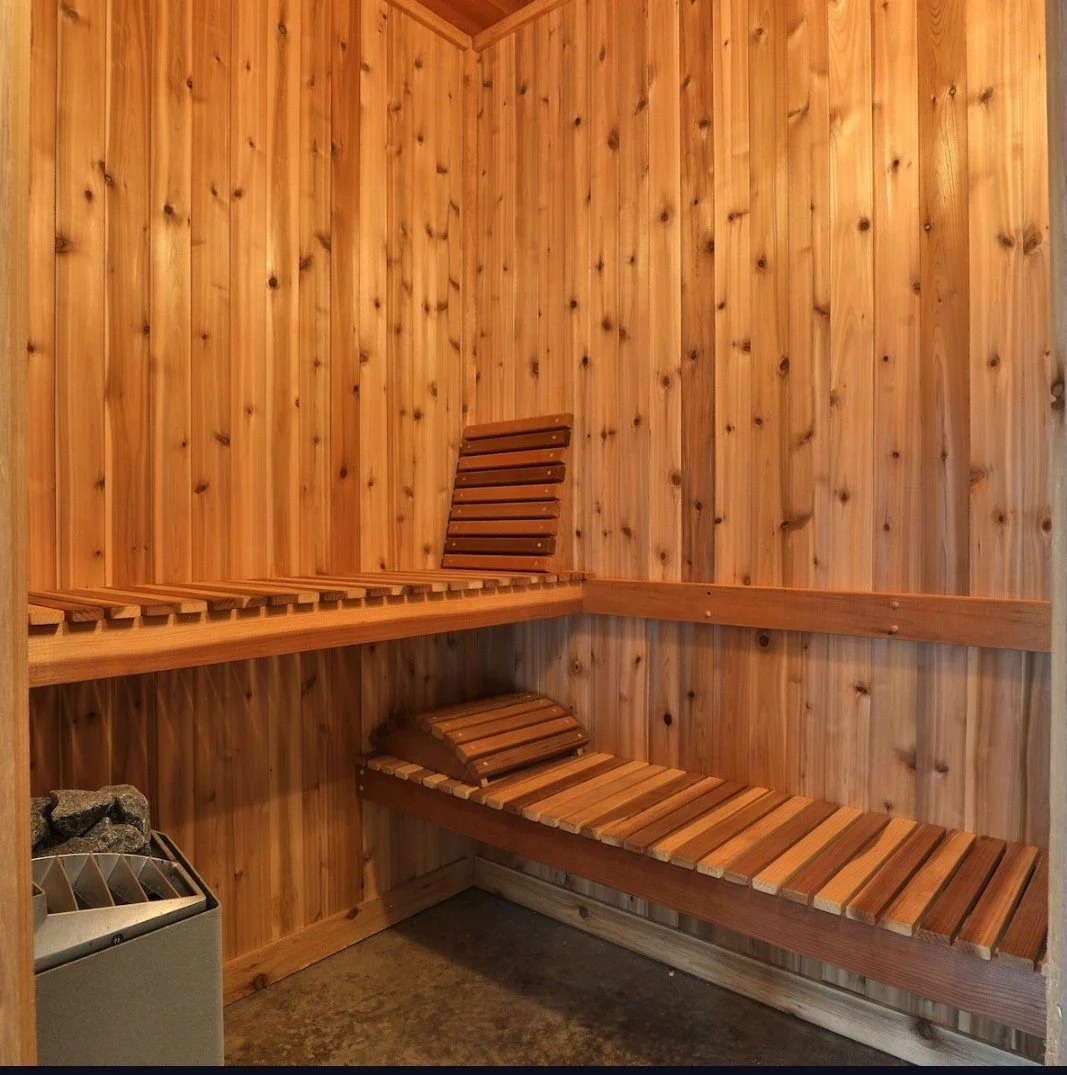 Wood-paneled sauna with wooden benches and a heater with rocks in the corner.