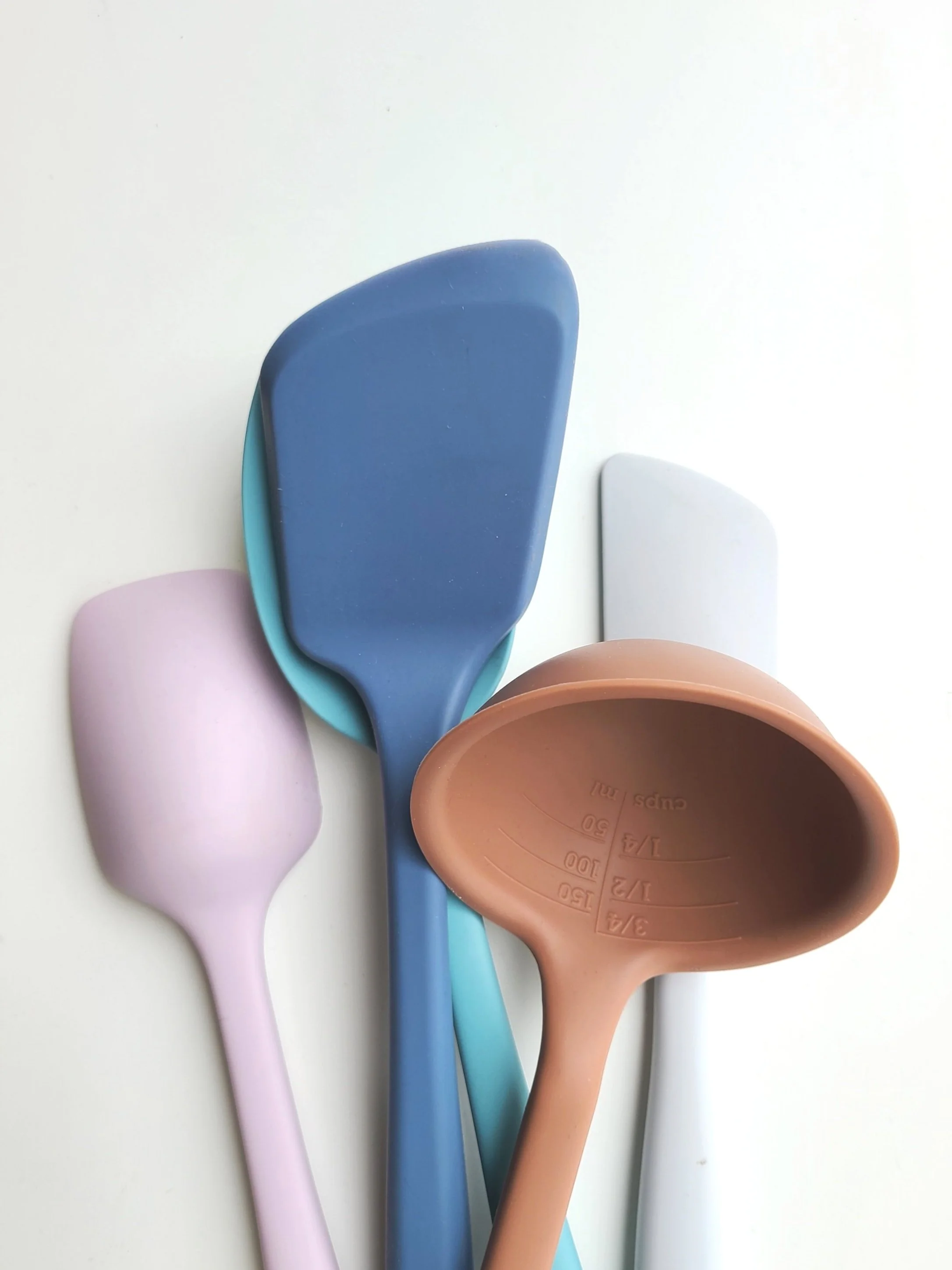 Colorful silicone measuring spoons in pink, blue, teal, and white, overlapping on a white surface.