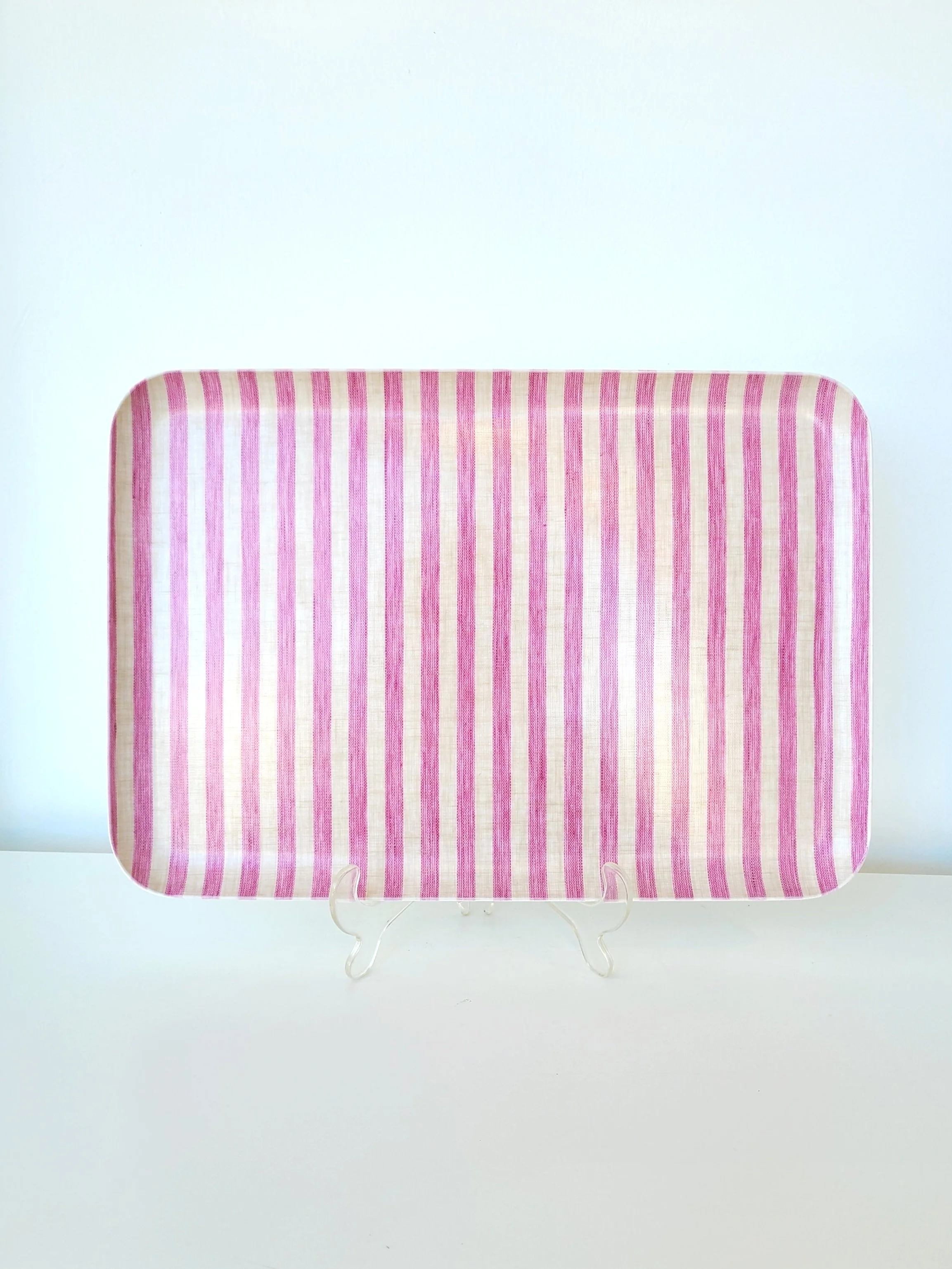 A rectangular pink and white striped fabric tray on a clear stand, placed on a white surface against a light background.