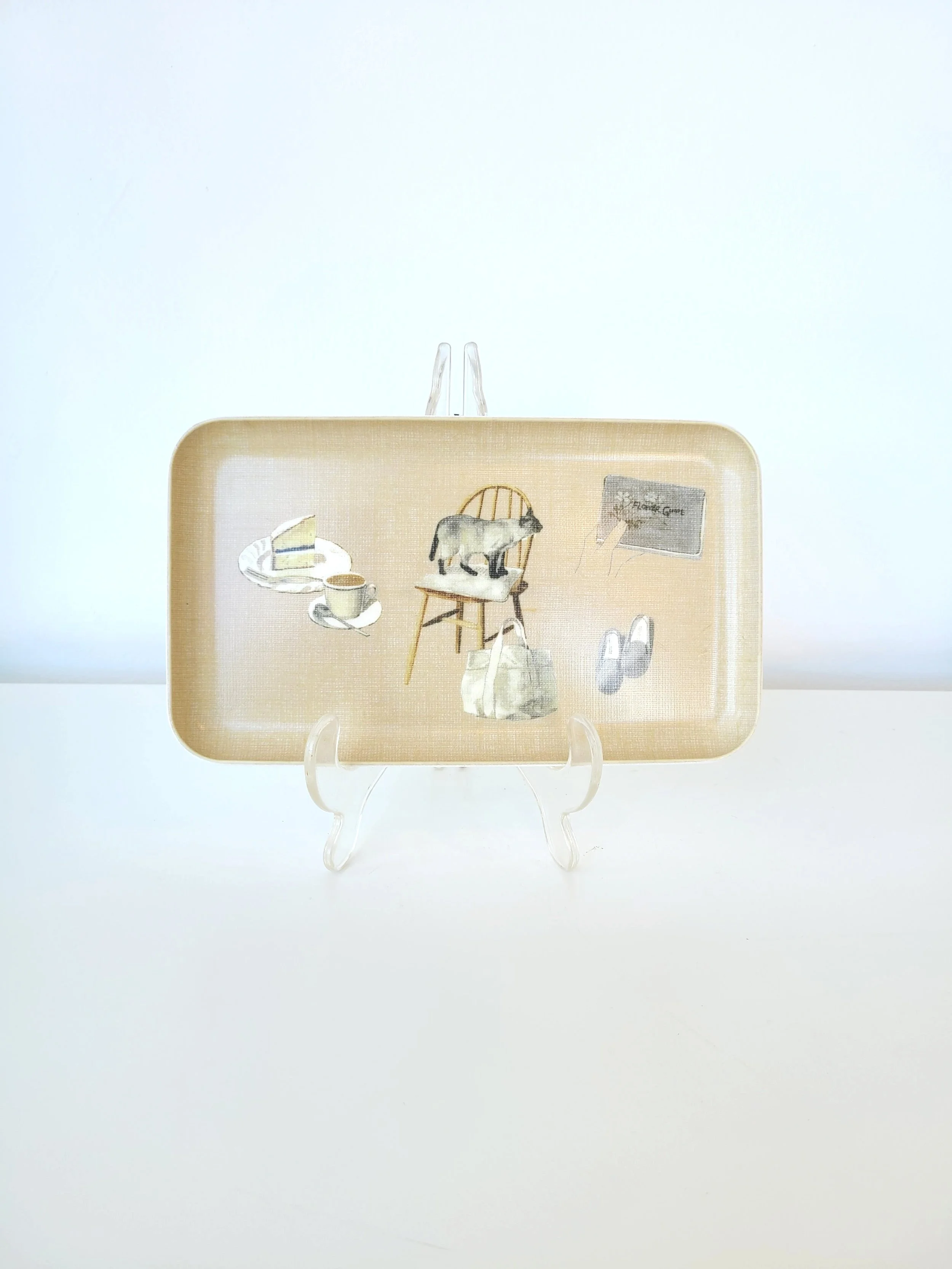 Decorative tray with illustrations of a slice of cake, a cup of coffee, a goat on a chair, a bag, shoes, and a chalkboard reading 'Flower Shop' on a display stand