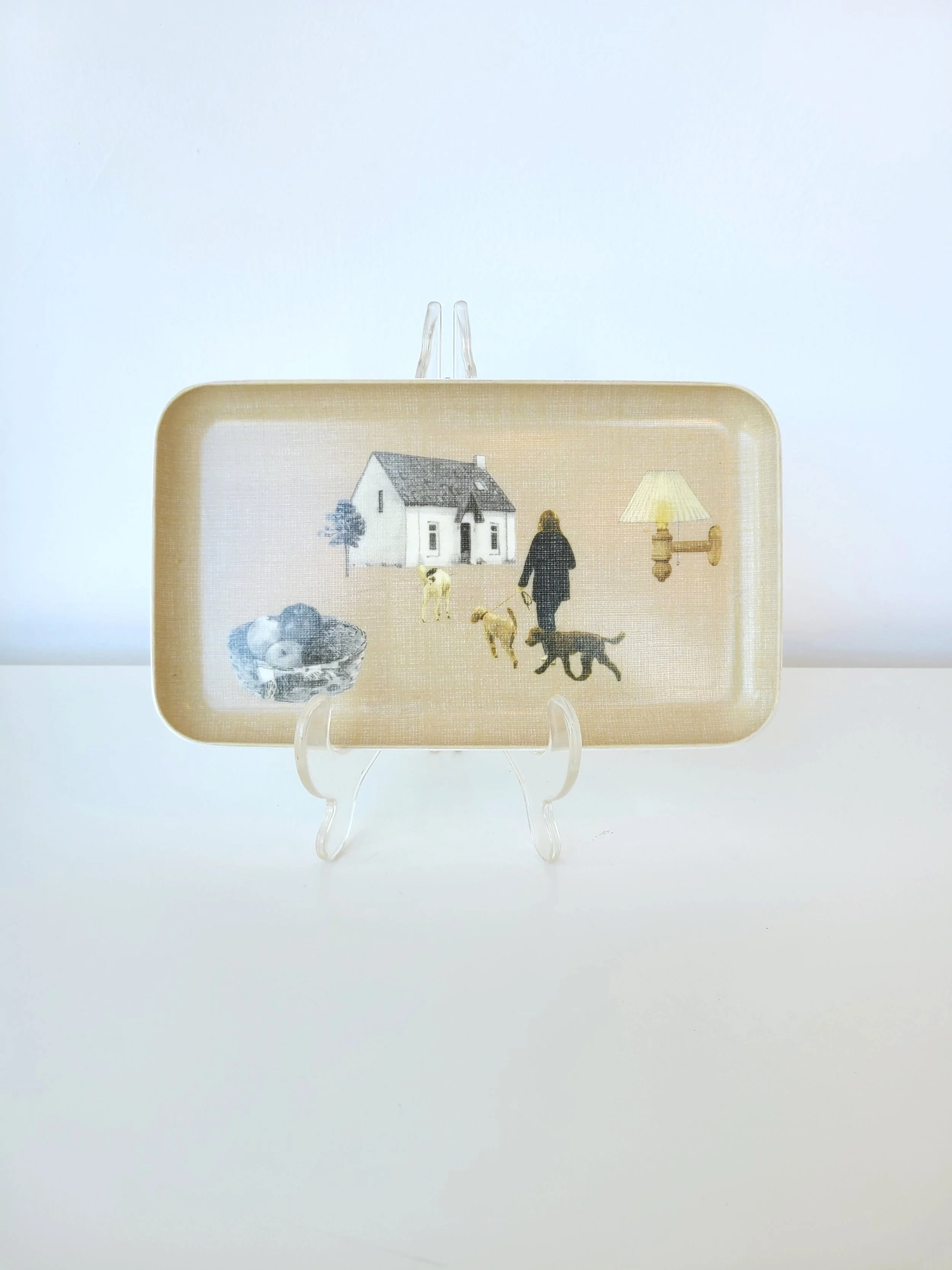 Decorative rectangular tray with a house, a woman walking dogs, a bowl of birds, a wall lamp, on a clear plastic stand