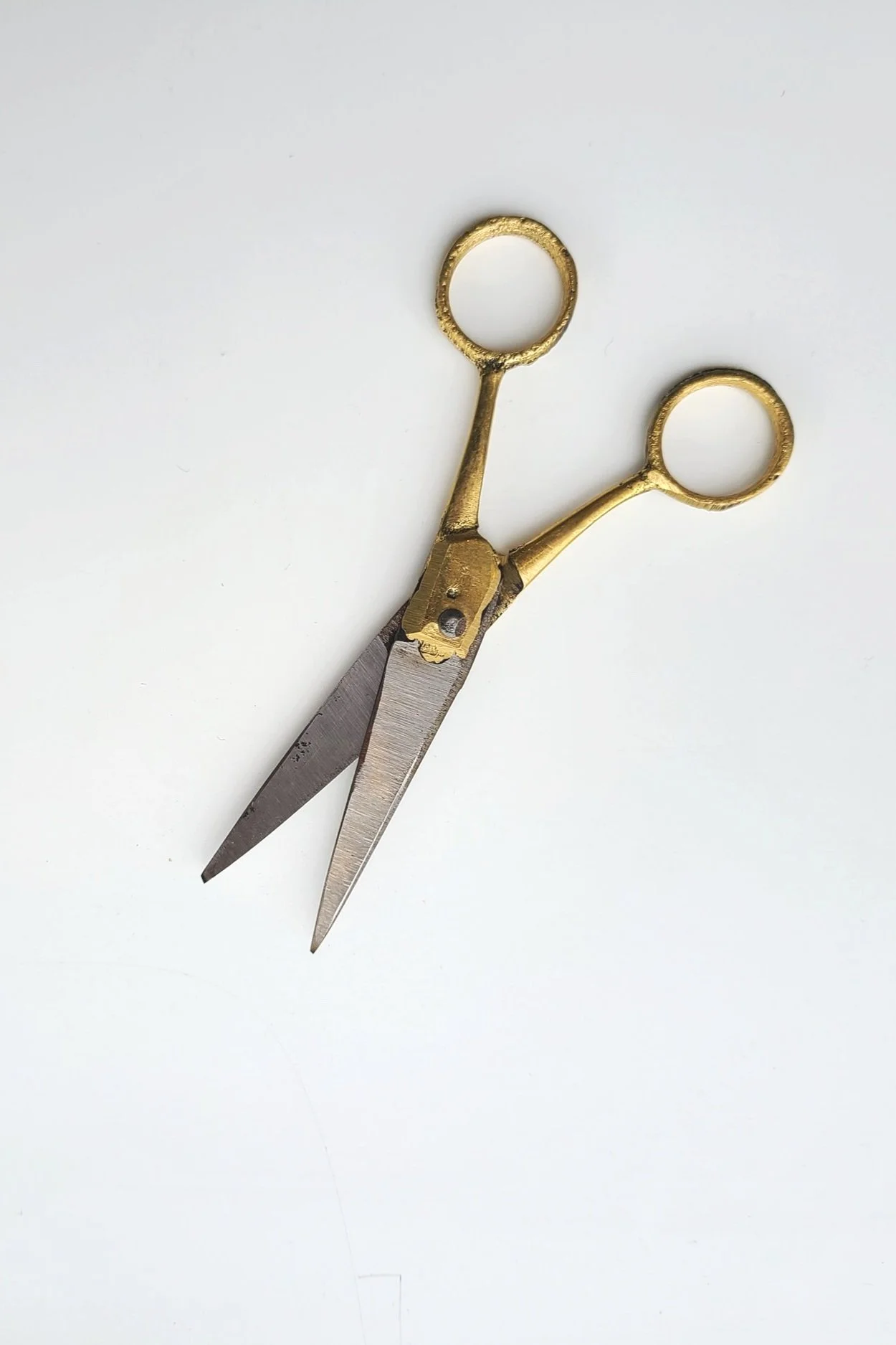 A pair of scissors with gold-colored handles and metal blades resting on a white surface.