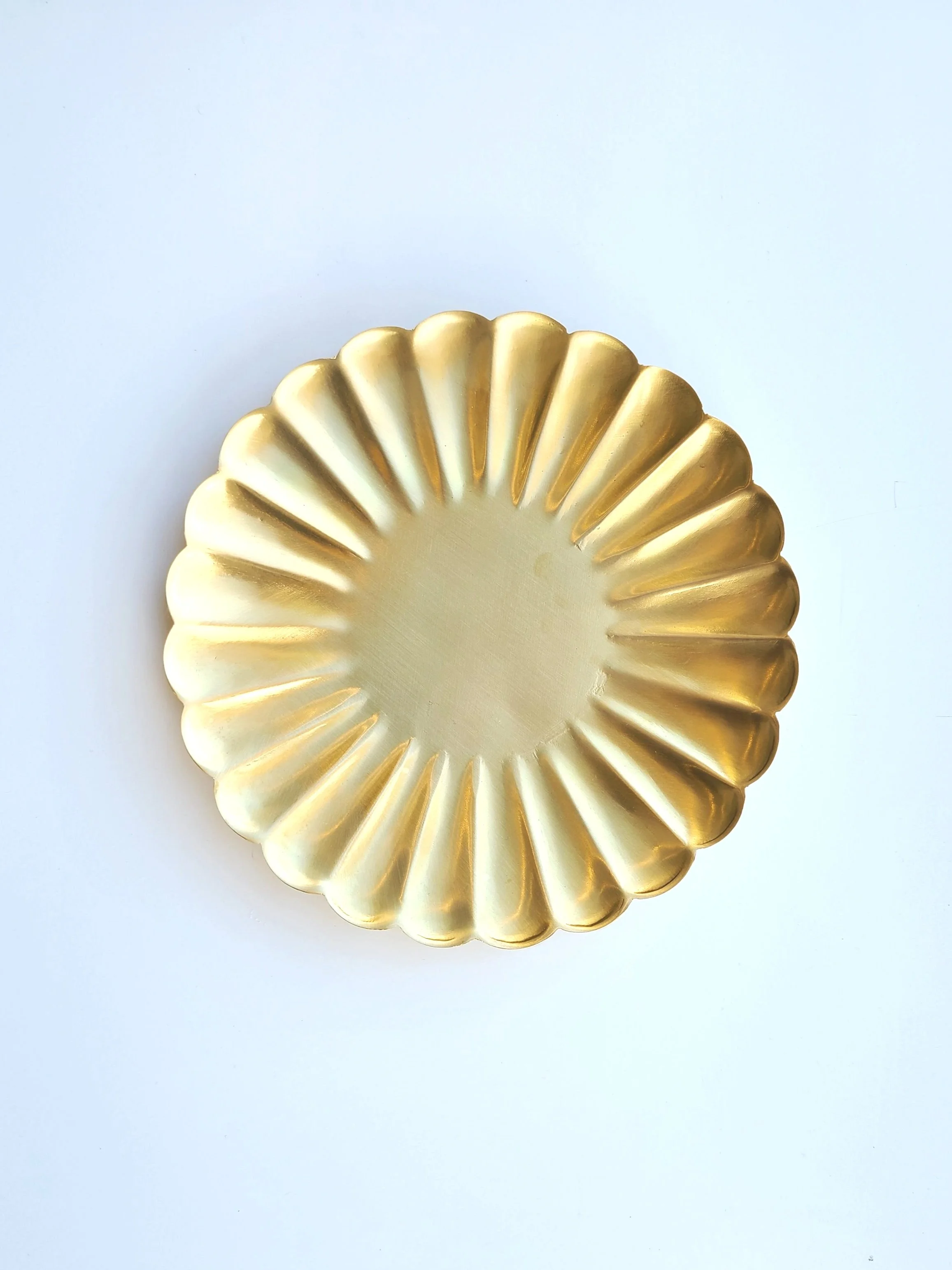 A round gold decorative plate with scalloped edges on a white background.
