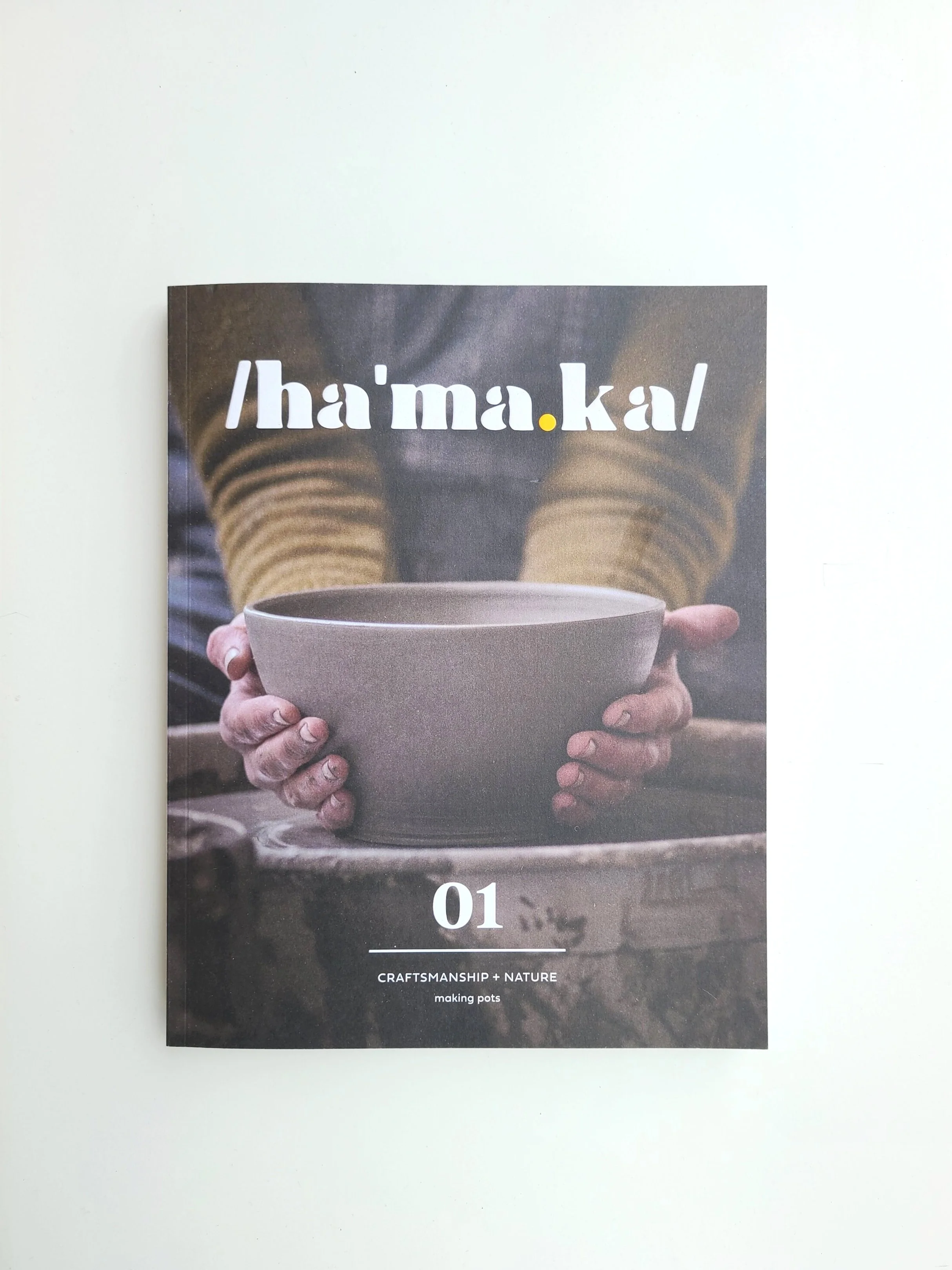 A magazine titled 'hama.kal' with a photograph of a person holding a pottery bowl. The person is wearing a brown and yellow striped sweater.