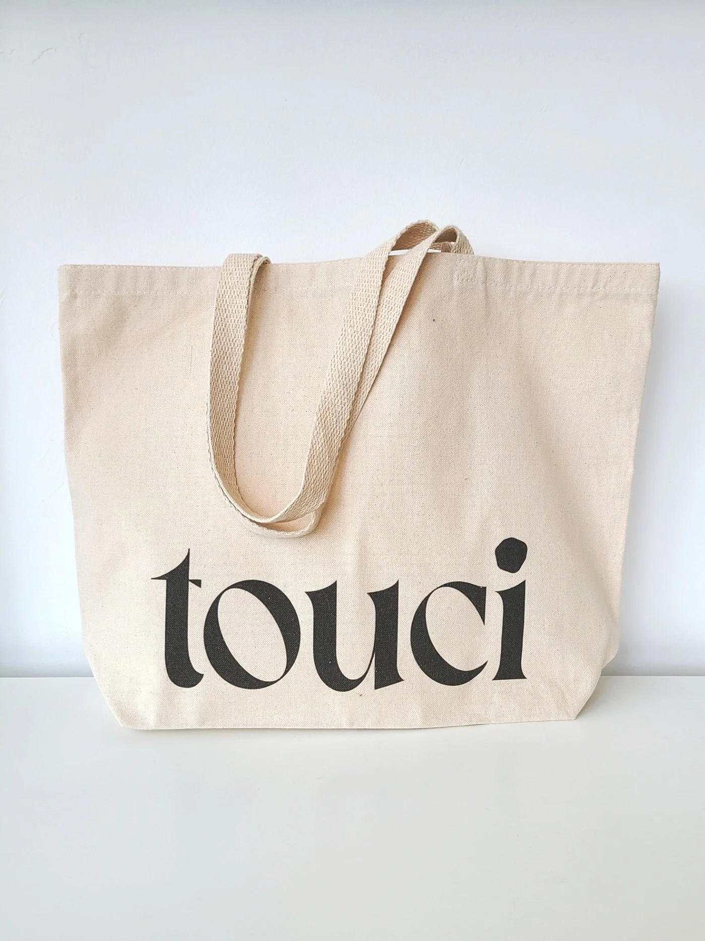 A beige tote bag with black text that says 'toui' printed on it, placed against a white background.