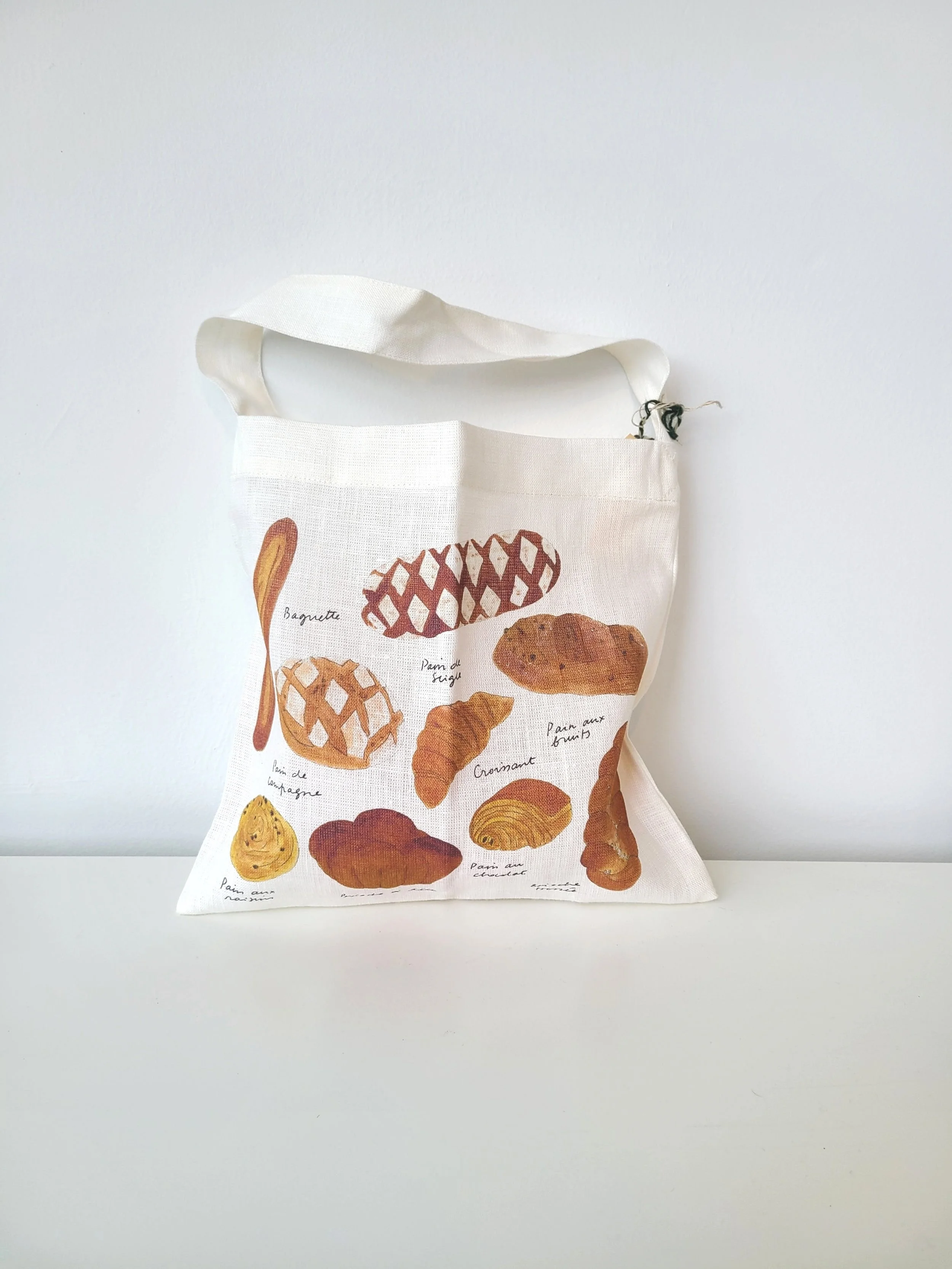 A white tote bag with illustrations of various types of French bread and pastries, each labeled with their names.