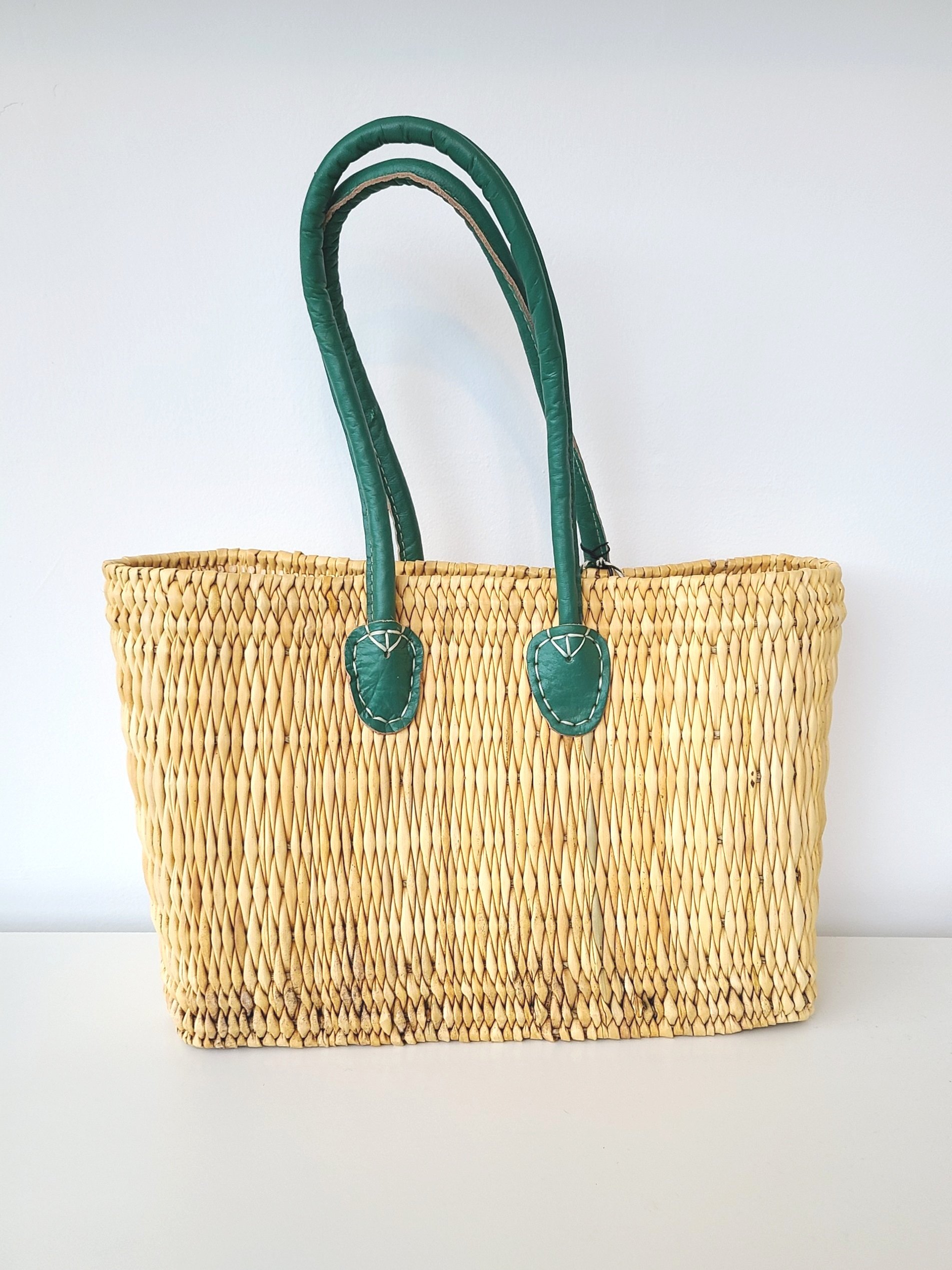 A woven straw tote bag with green leather handles