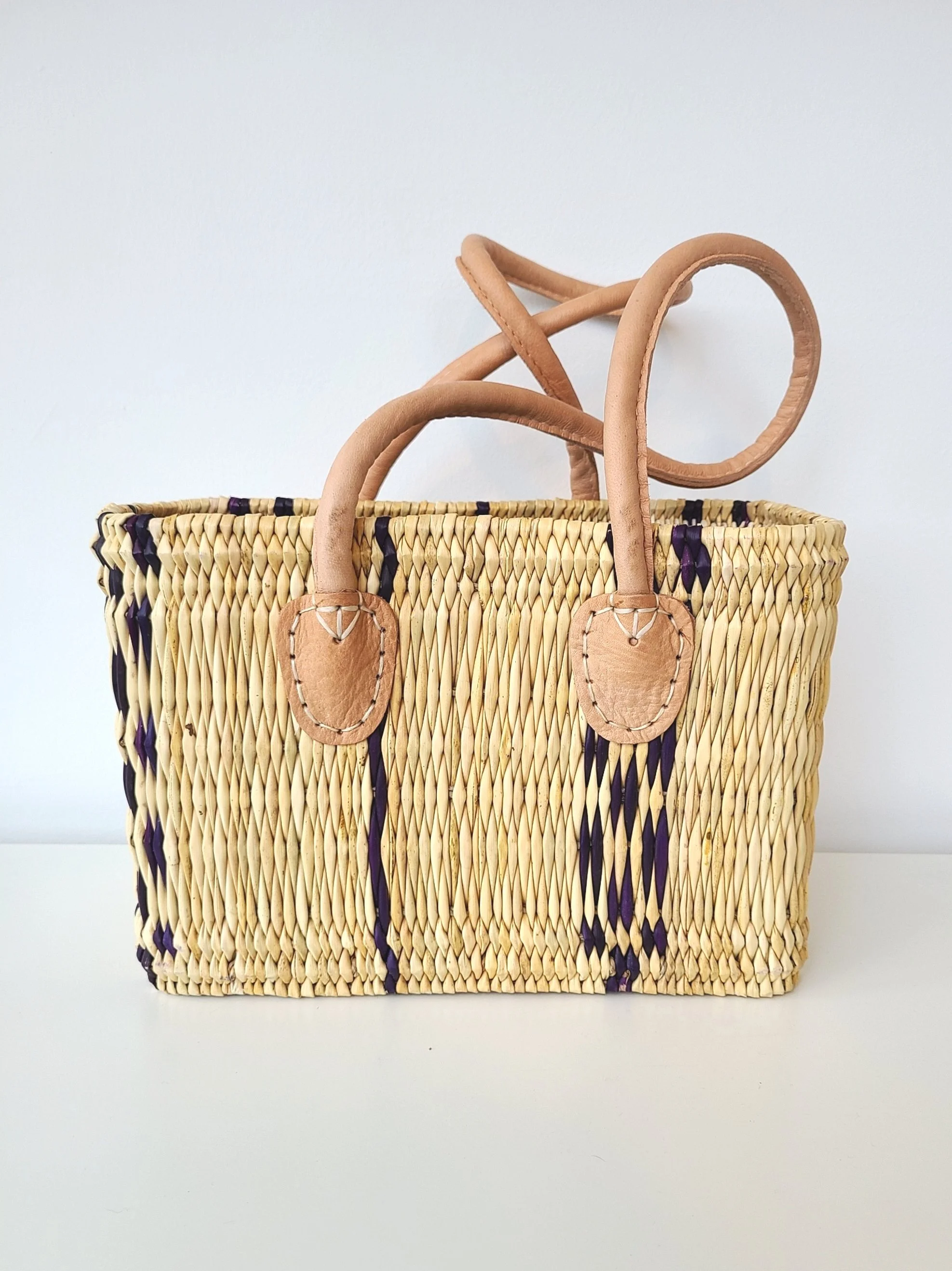 Woven straw handbag with tan leather handles and accents, featuring dark purple vertical stripes.