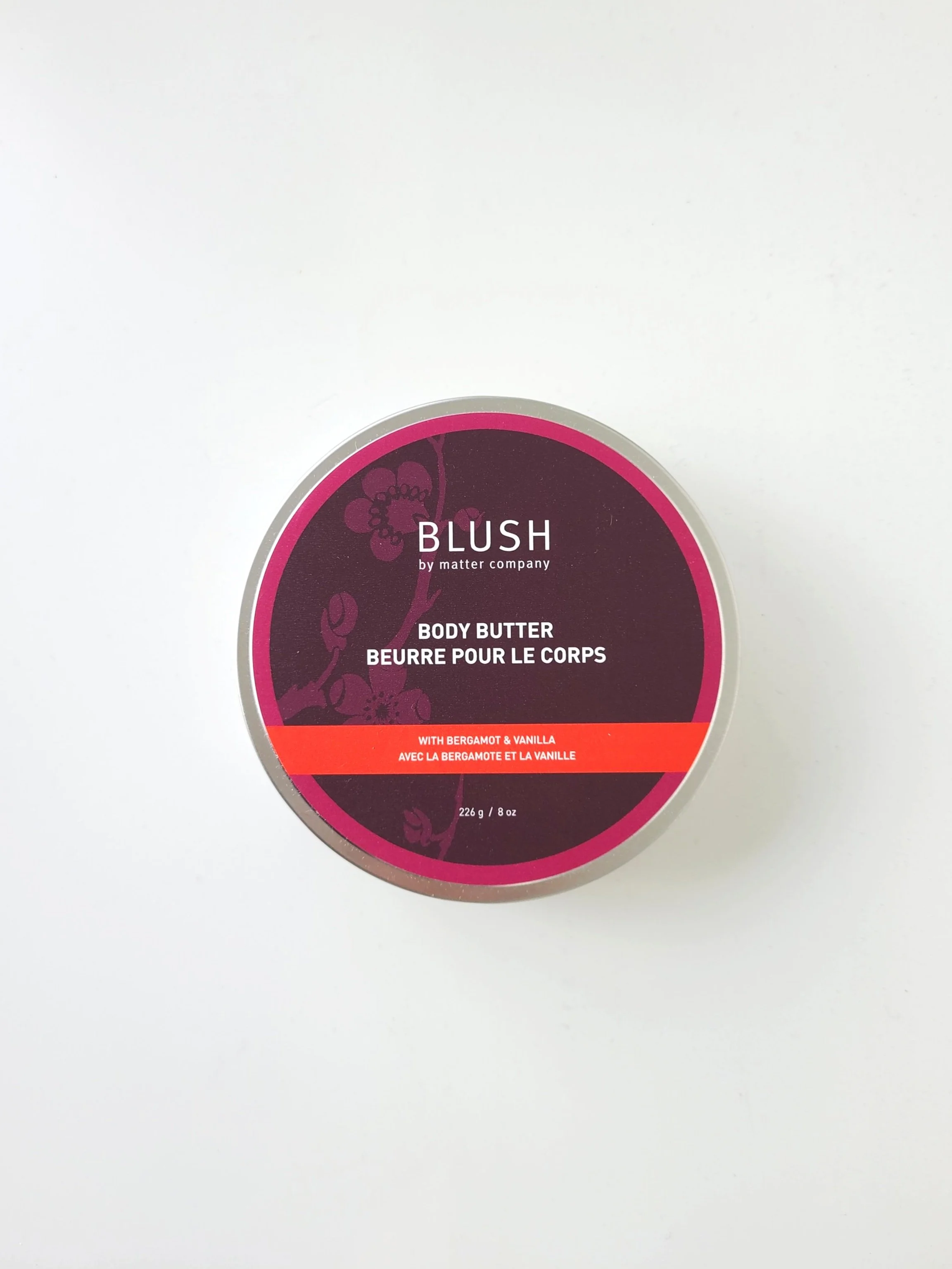 A round container of BLUSH body butter with bergamot and vanilla scent, placed on a white surface.
