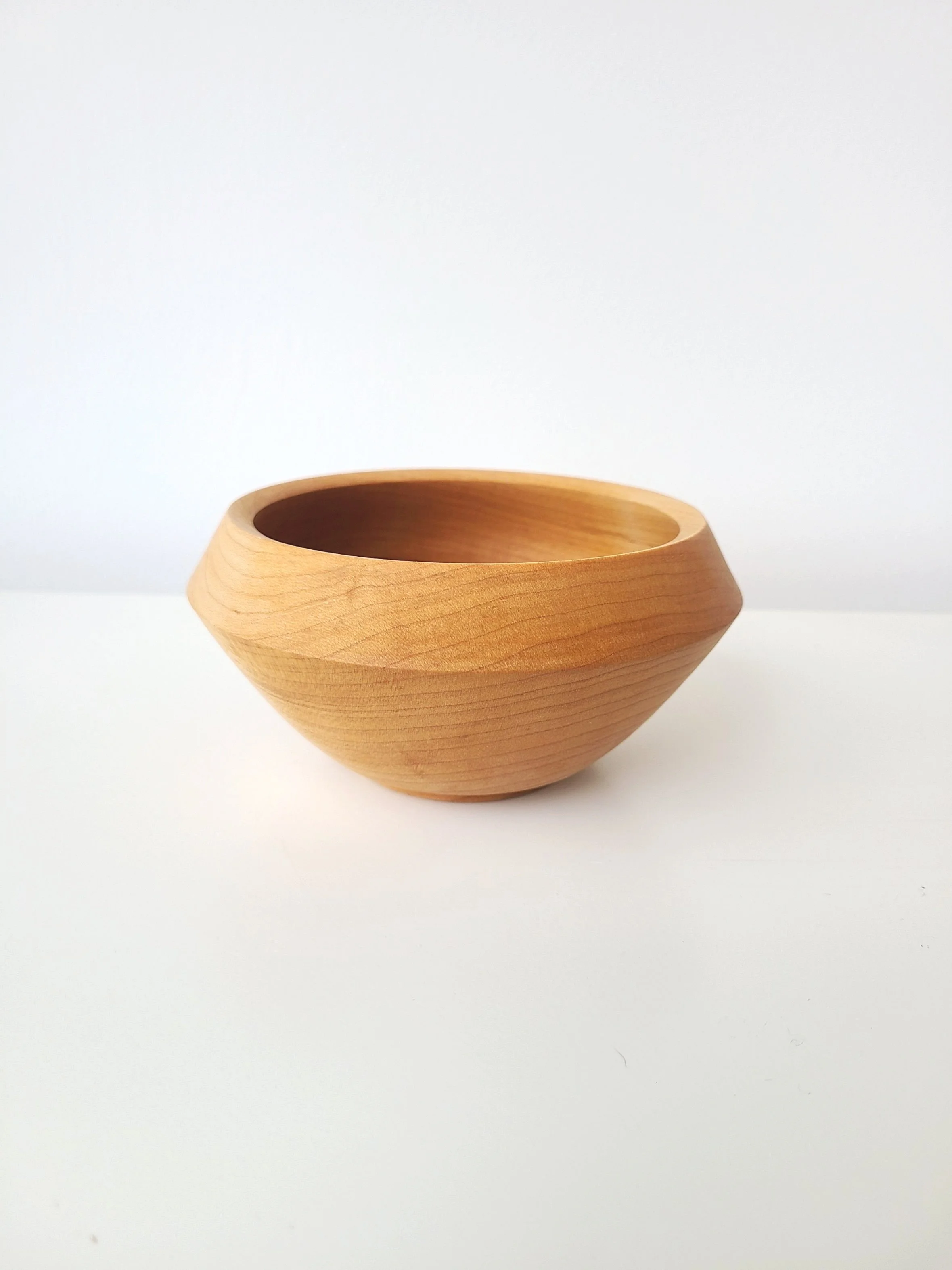 A wooden bowl with a smooth, natural finish placed on a white surface with a plain white background.