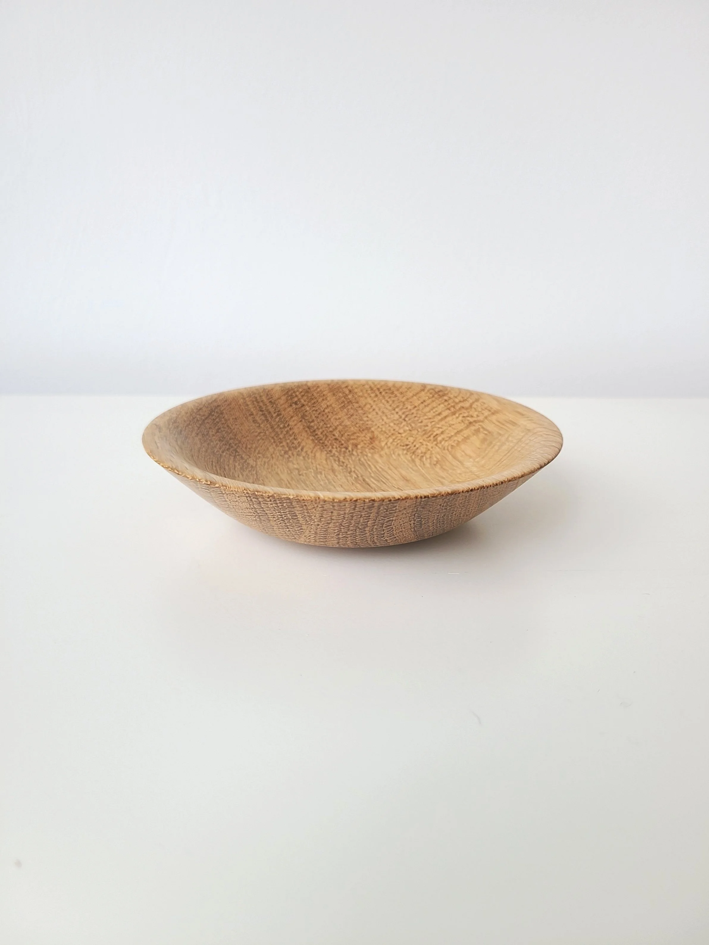 A round wooden bowl with a natural finish on a white surface against a white background.