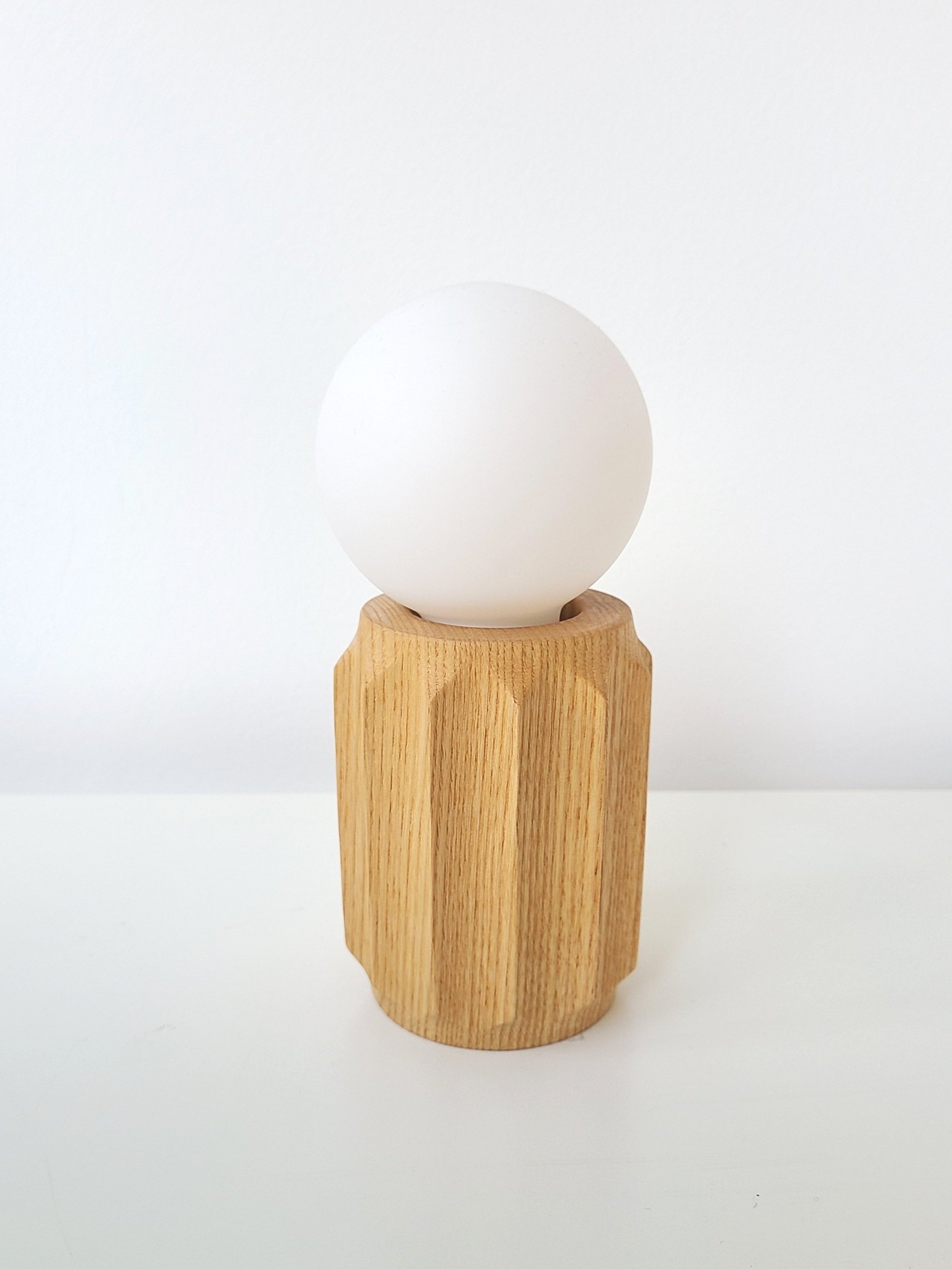 A white egg resting on a wooden egg holder placed on a white surface with a plain white background.