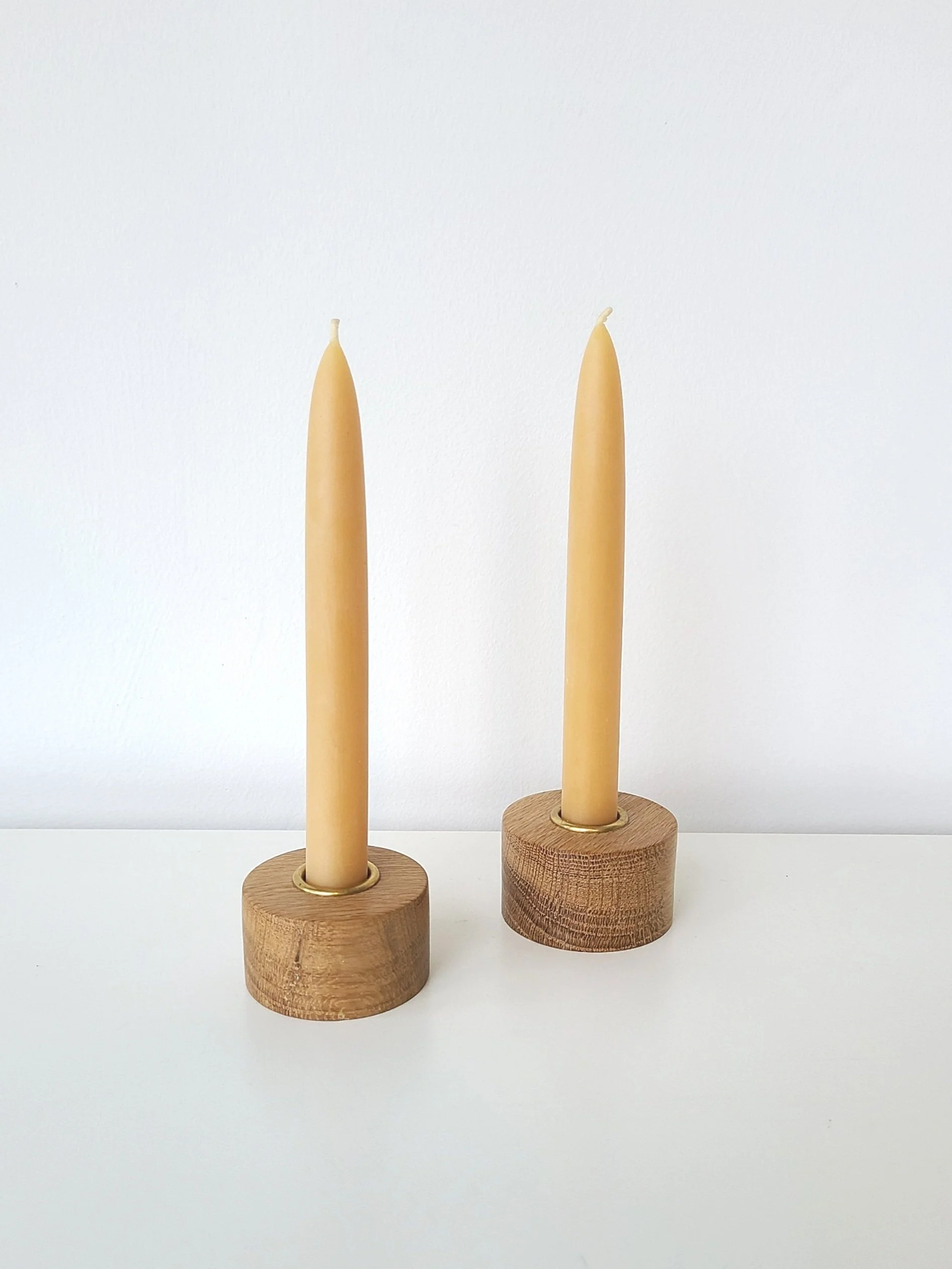 Two beige candles in wooden bases on a white surface with a plain white background.