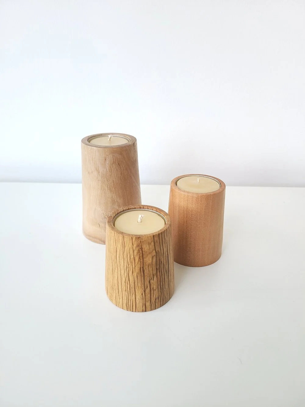 Three wooden candle holders with white candles on a white surface against a white background.