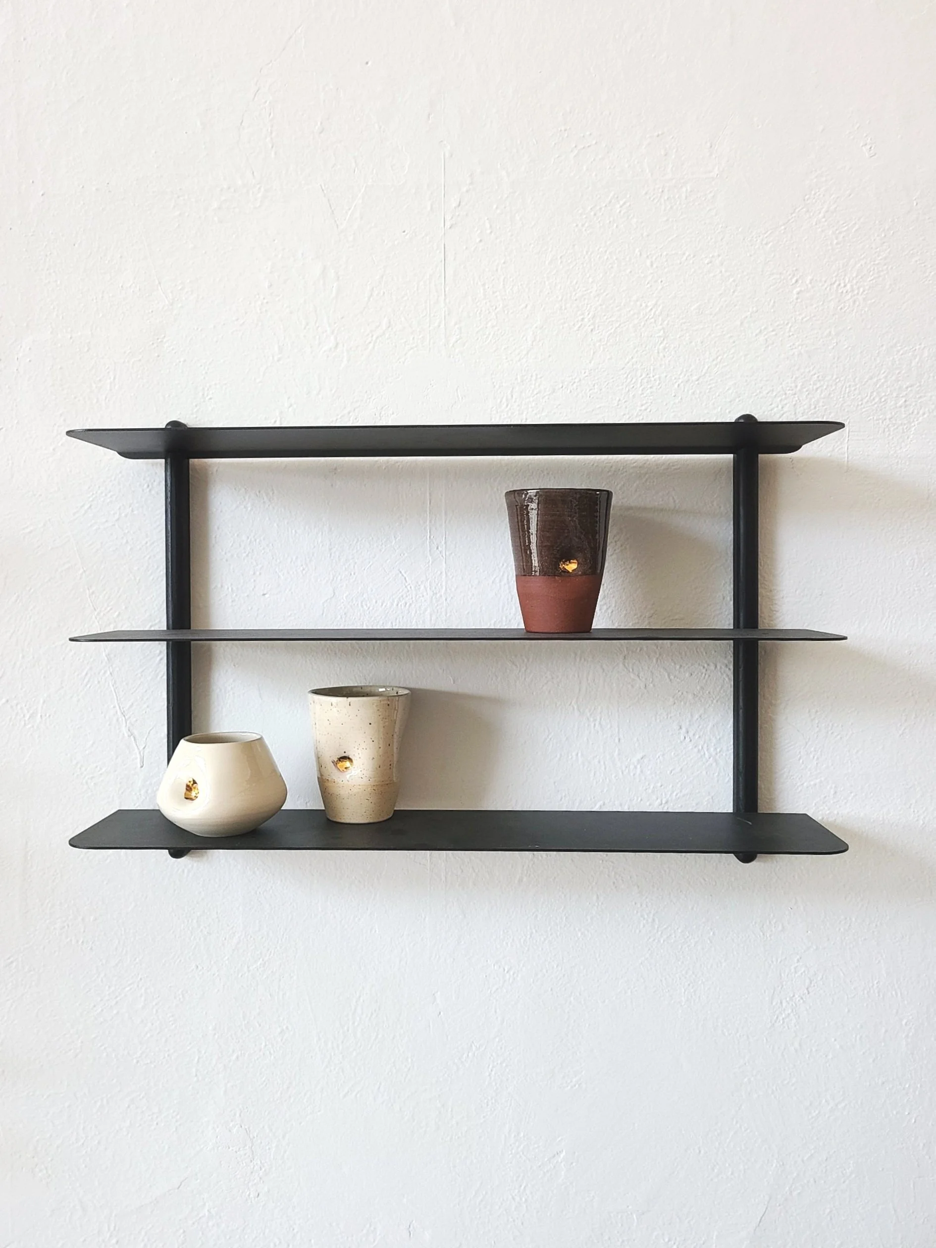 Black wall shelf with three ceramic vases on a white wall.