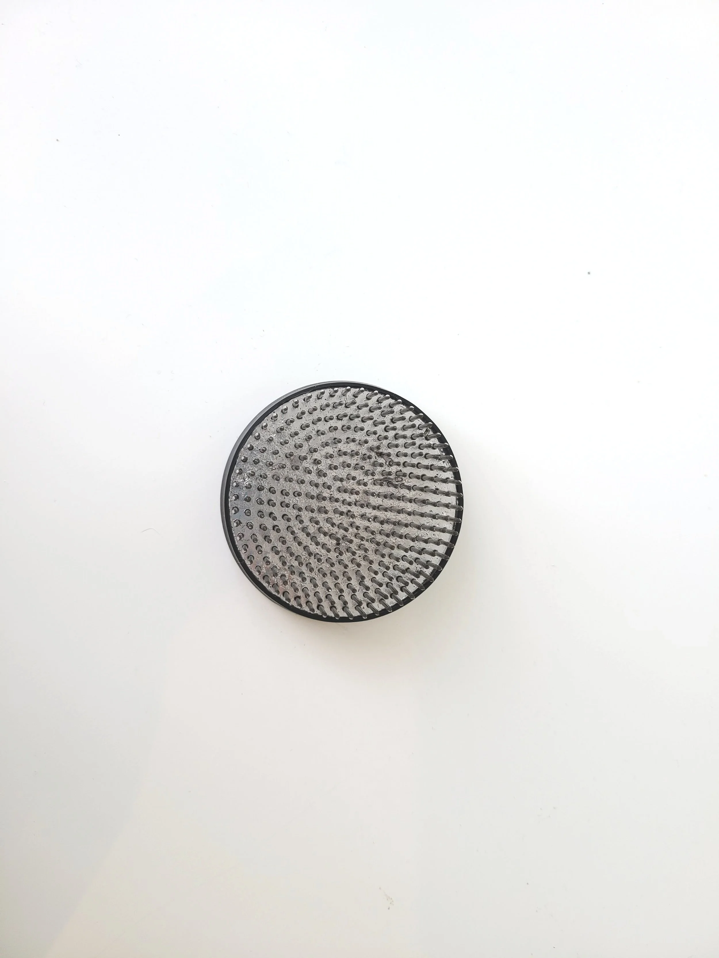 A black hairbrush with a circular shape and bristles, positioned on a white surface.