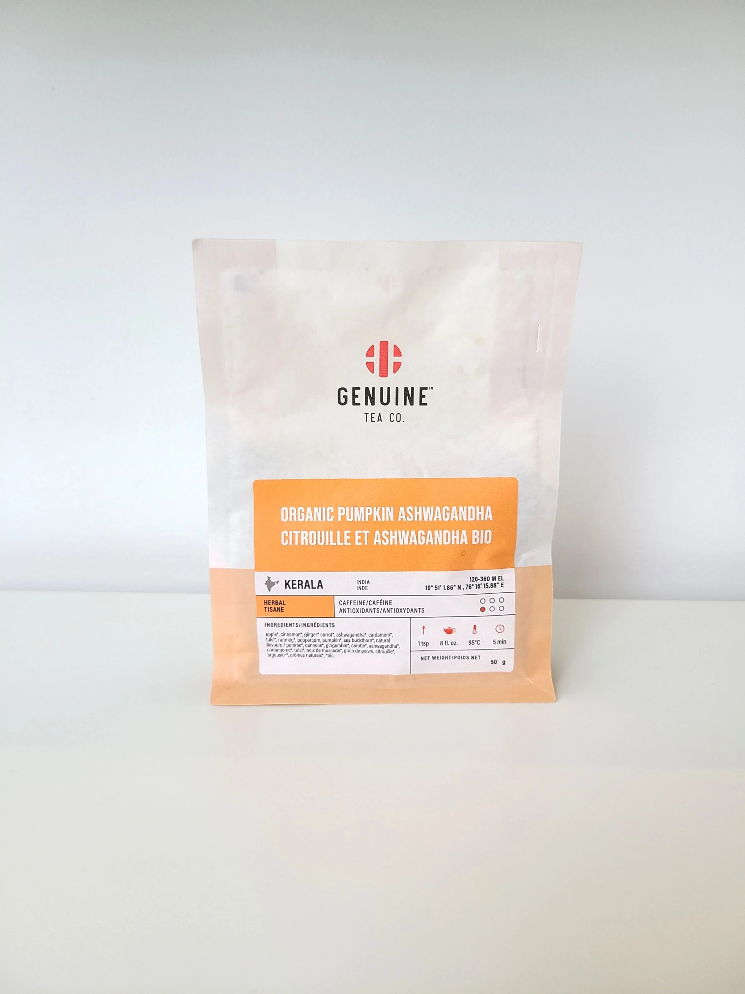A packet of Genuine Tea Co. organic pumpkin ashwagandha tea, with a white and orange design, placed on a white surface against a light gray background.