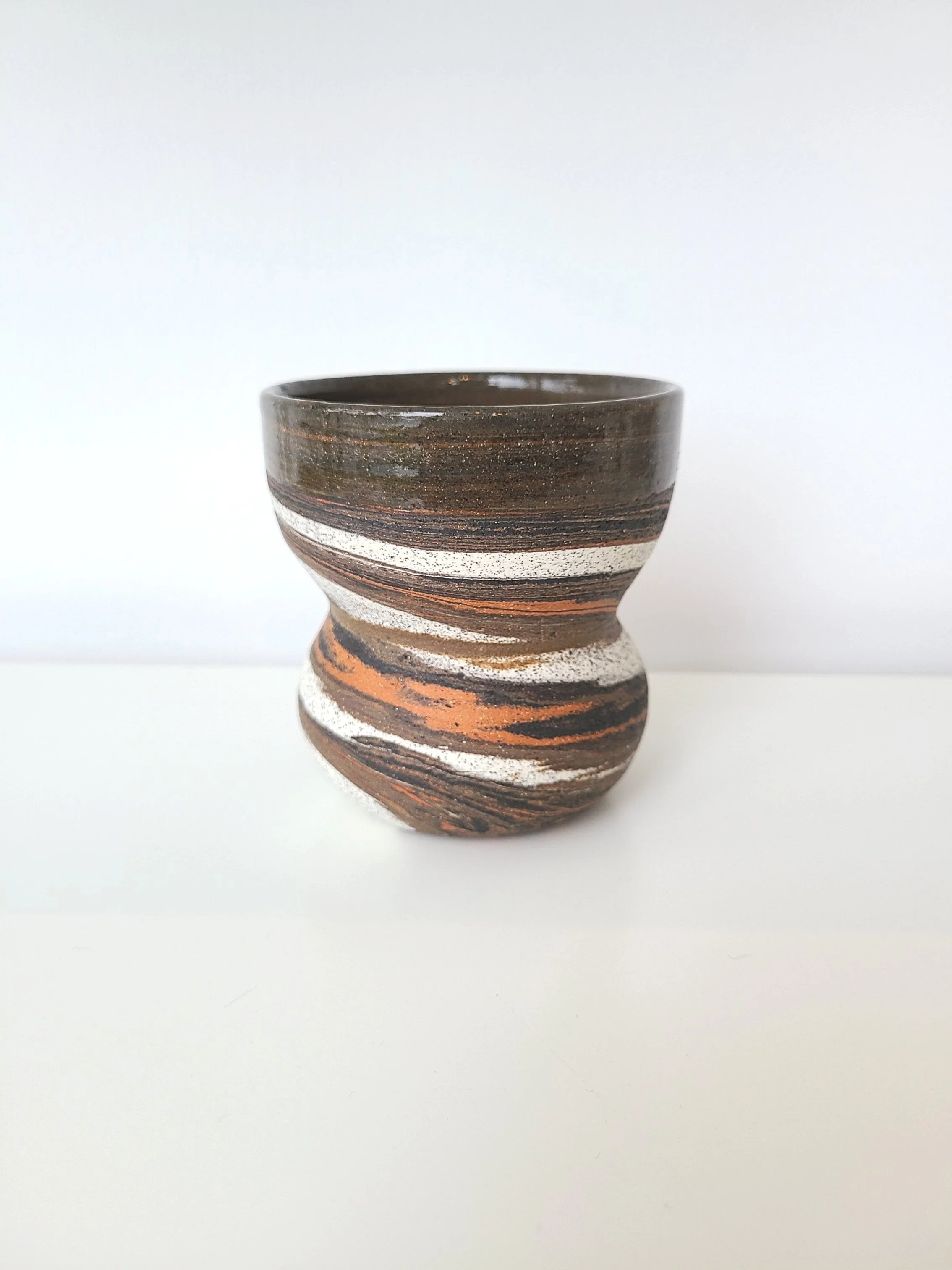 Ceramic cup with marble-like swirls of brown, black, white, and orange on a white surface against a plain white background.