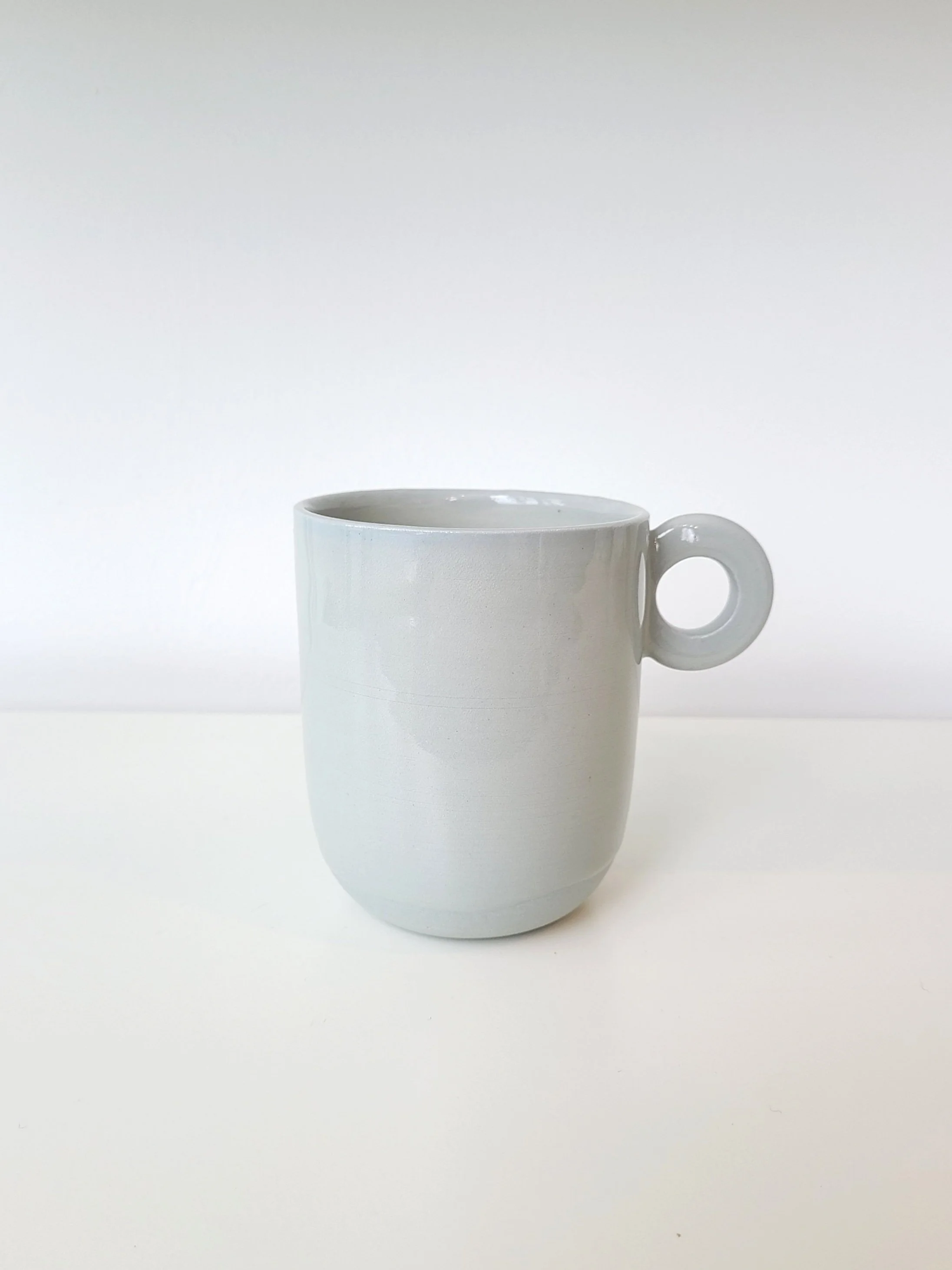 White ceramic mug with a round handle on a white surface against a white background.