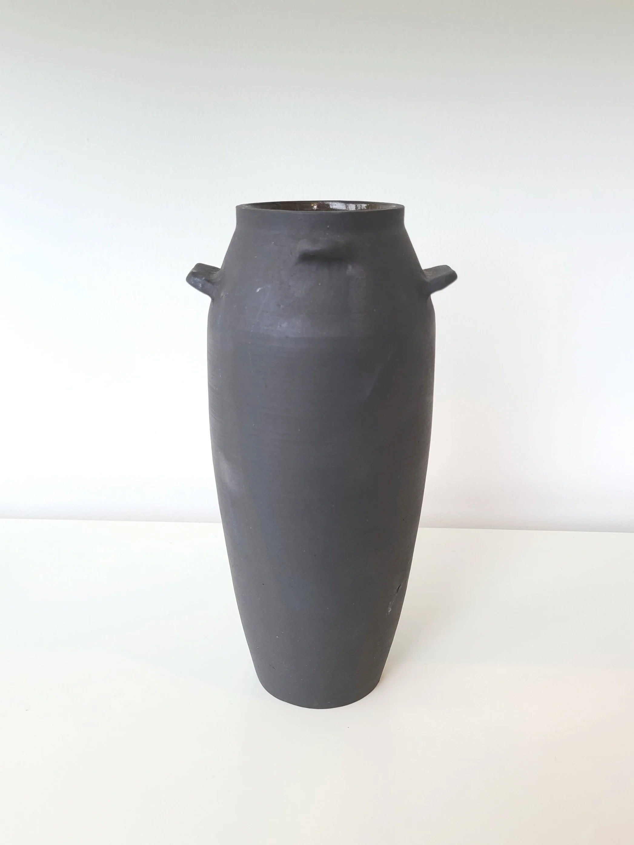 A tall black ceramic vase with two small handles on the sides, placed against a plain white background.