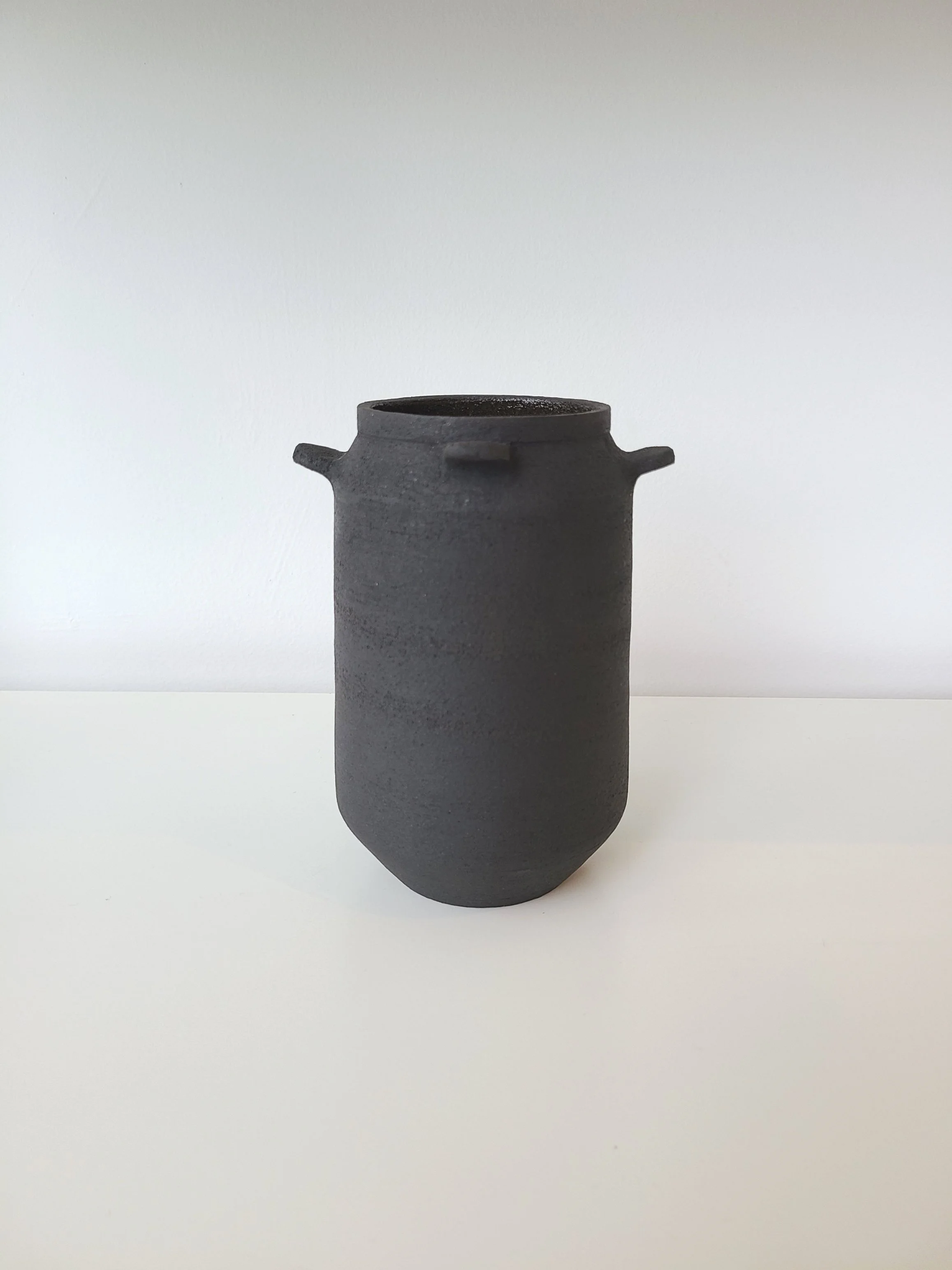 A minimalist black ceramic vase with two small handles, set against a plain white background.
