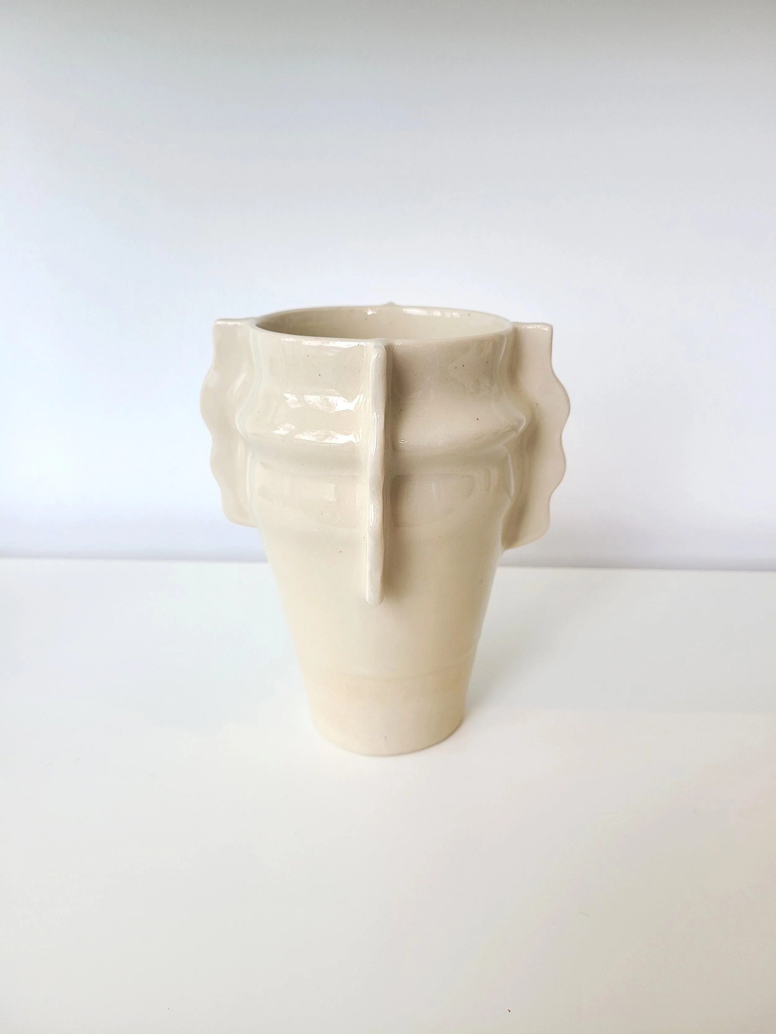 Cream-colored ceramic vase with textured, raised vertical ridges, placed on a white surface with a plain white background.